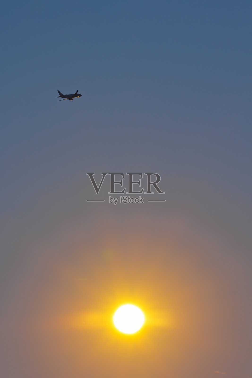 一架飞机在万里无云的天空中的剪影,背景是太阳照片摄影图片