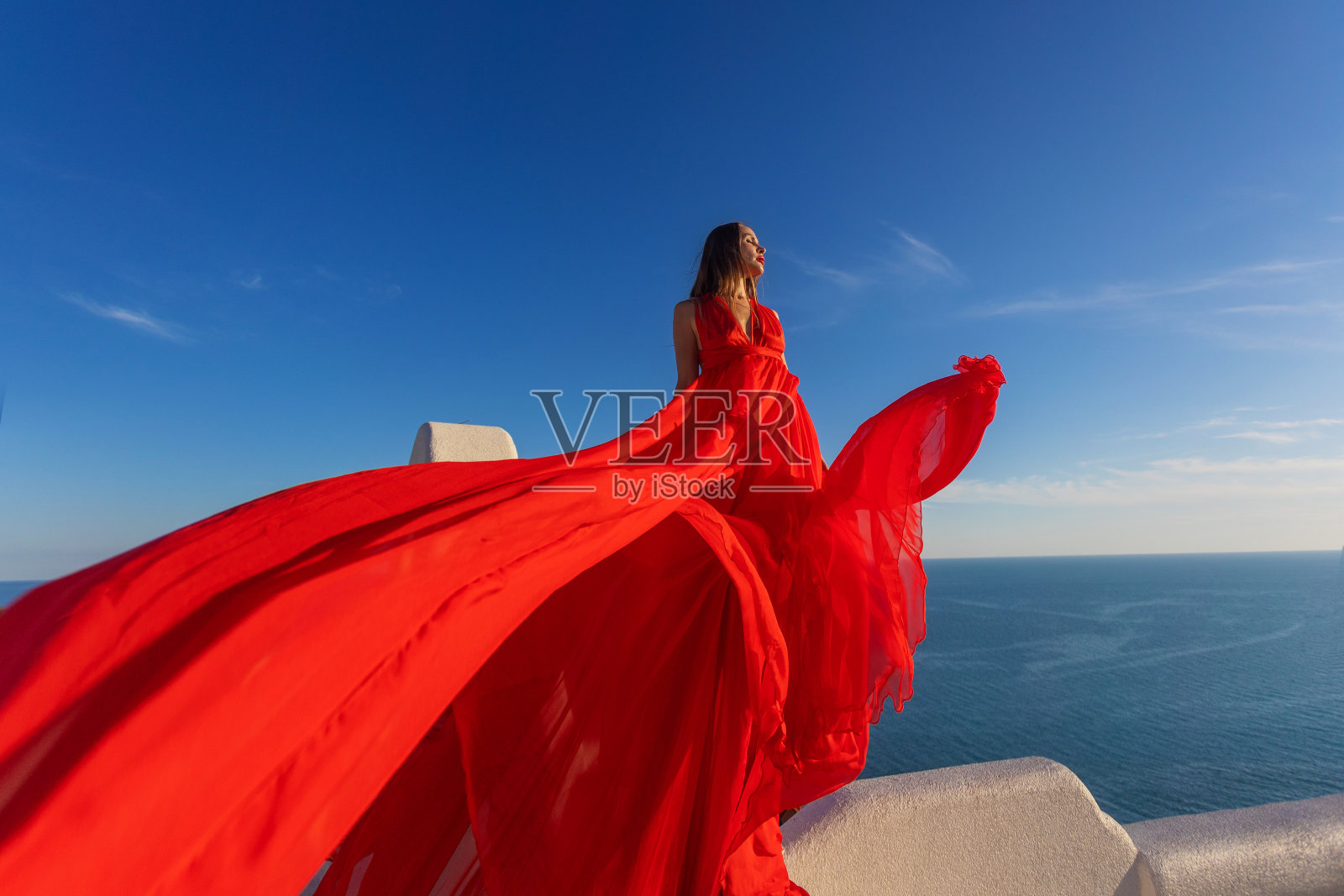 魅力的照片。女孩在大海的背景下挥舞着一件飘逸的红色连衣裙照片摄影图片