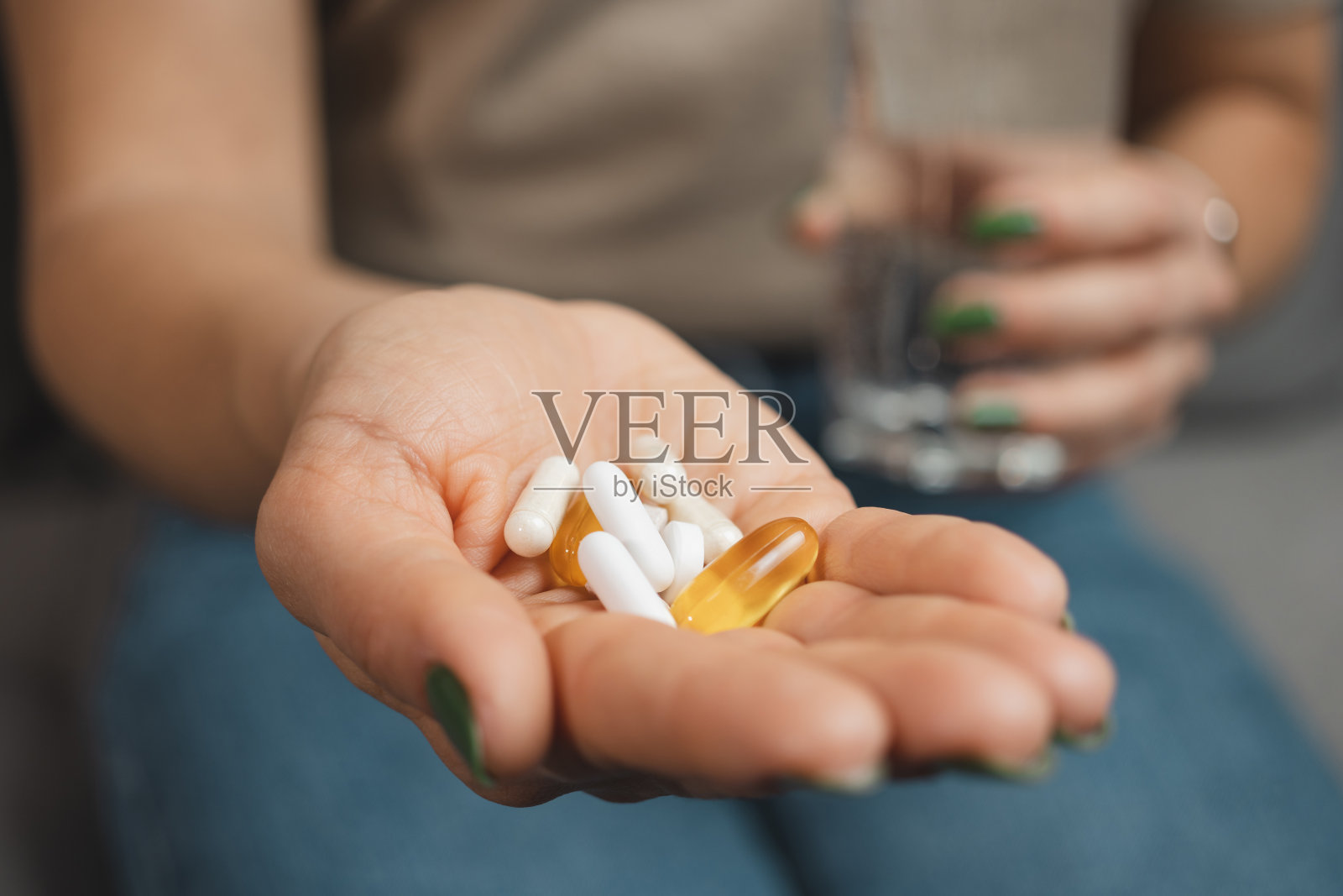 年轻女子手里拿着各种药片和胶囊,手里拿着一杯水,特写镜头照片摄影图片