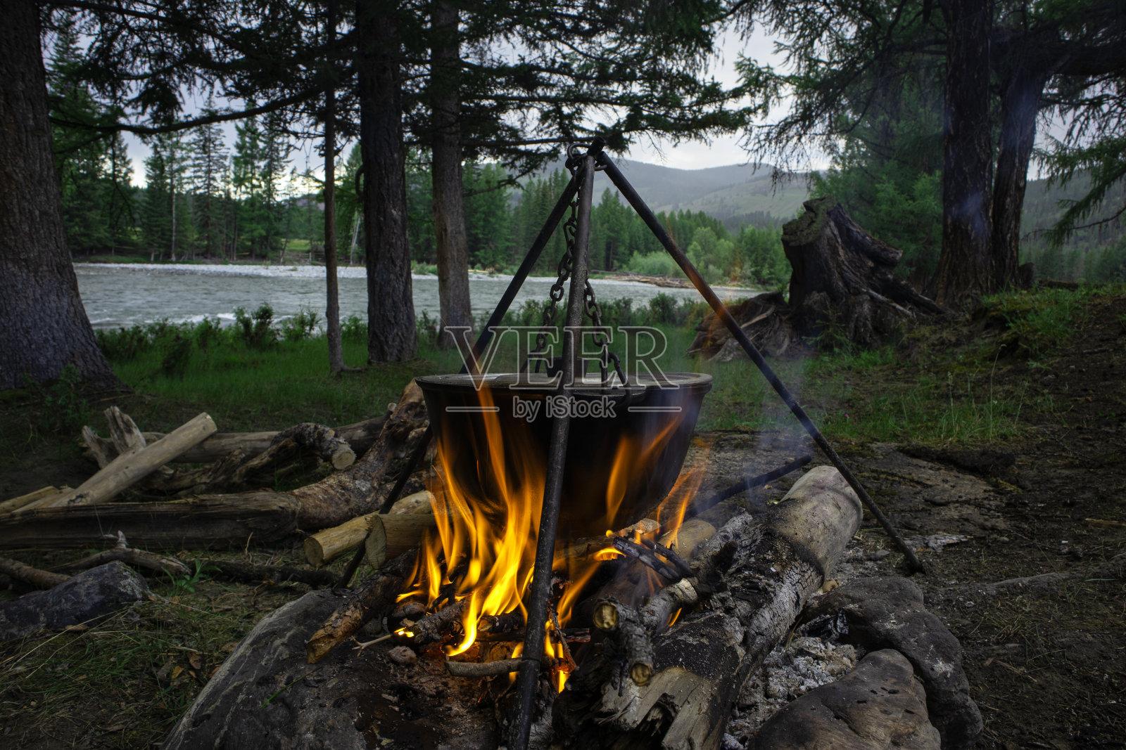 游客们在篝火上的露营锅里准备午餐。在户外山河岸边的森林里做饭。旅行营地,营火地点。照片摄影图片