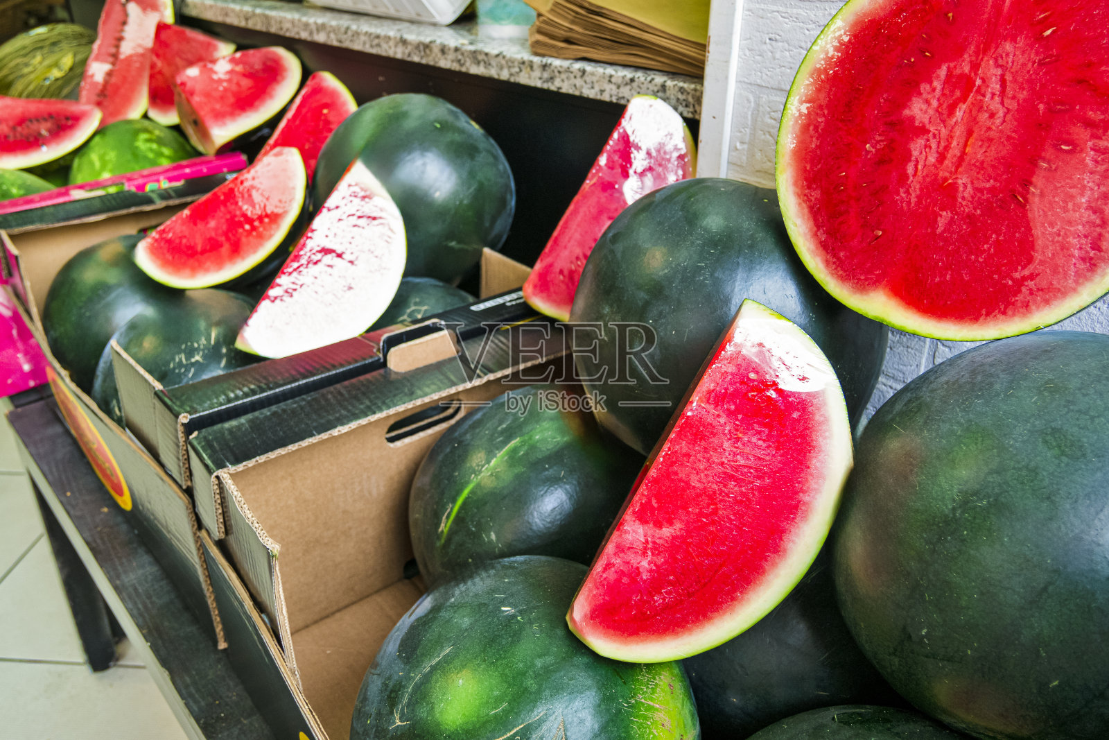 大量的绿色甜瓜和切好的西瓜放在木桌上,在户外出售。照片摄影图片