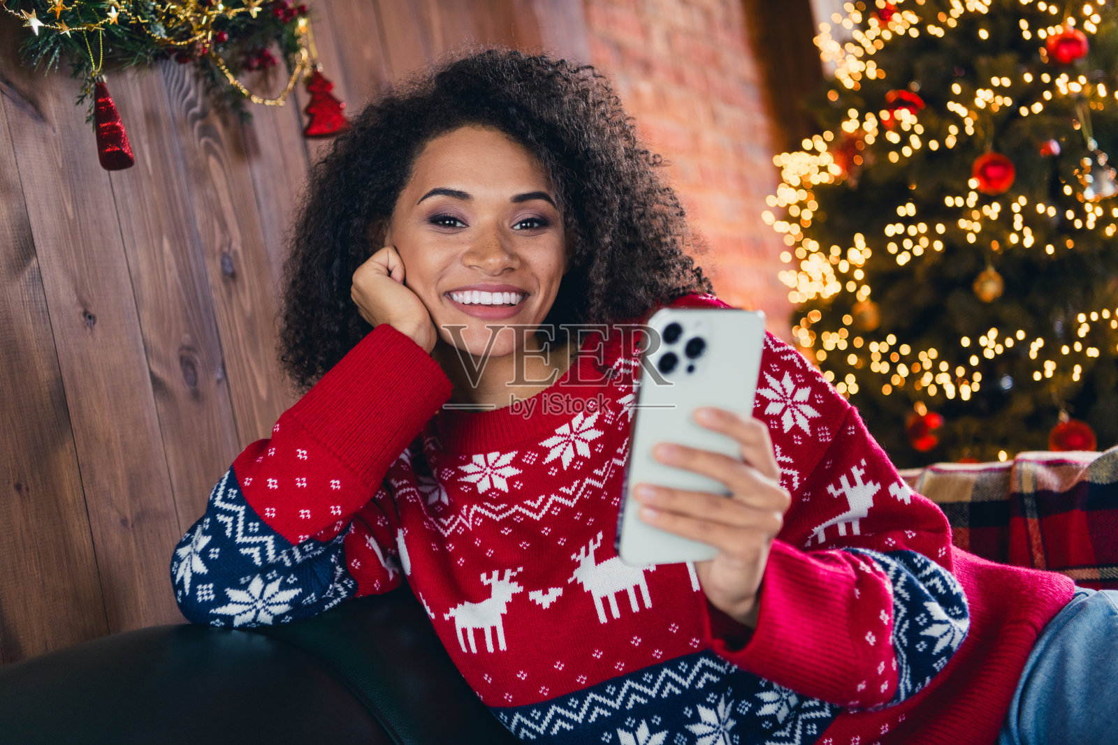 有趣的画像和平的人牙齿微笑坐在沙发上使用智能手机享受童话般的圣诞时间公寓室内照片摄影图片