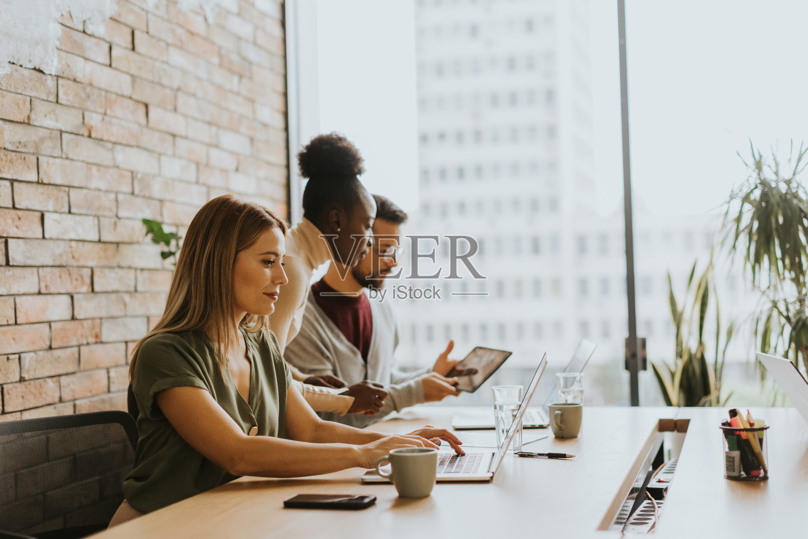 年轻的多民族创业团队在工业风格办公室的砖墙旁工作照片摄影图片