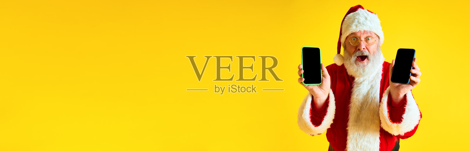 横幅。惊喜的是,长着长长的灰胡子的老人看起来像圣诞老人,展示着空白屏幕的手机,孤立的黄色背景和负空间。照片摄影图片