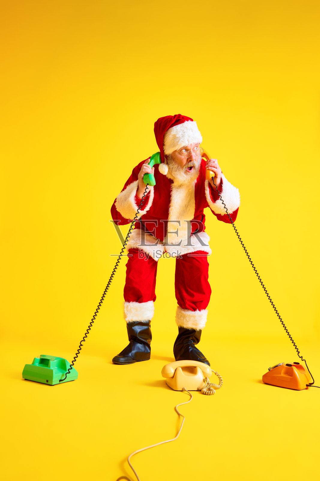 一名留着长胡子的老人接到了孩子们的复古电话,他们正在等待黄色工作室背景下的礼物。照片摄影图片