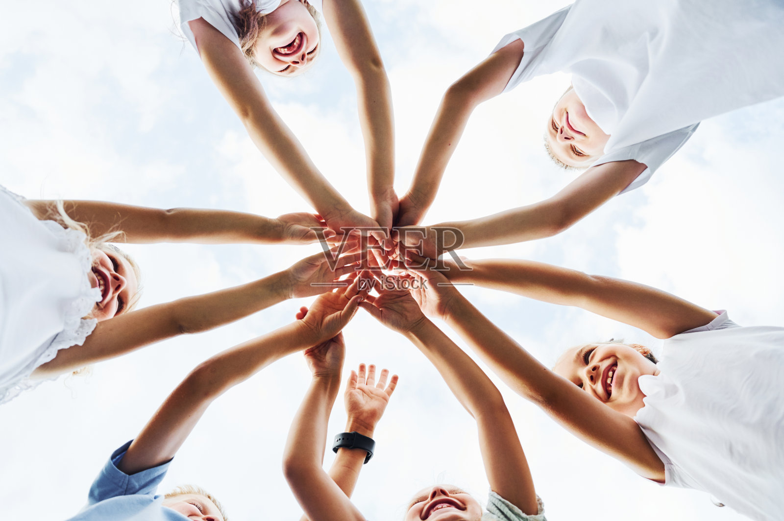 从下面看孩子们手牵着手。映衬着白色的天空照片摄影图片