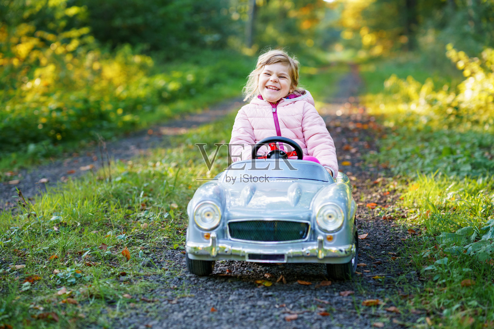 学前班的小女孩开着老式玩具车。快乐的孩子在户外玩耍。活跃的学龄前儿童在森林里享受温暖的秋日。笑容灿烂的孩子在玩耍照片摄影图片