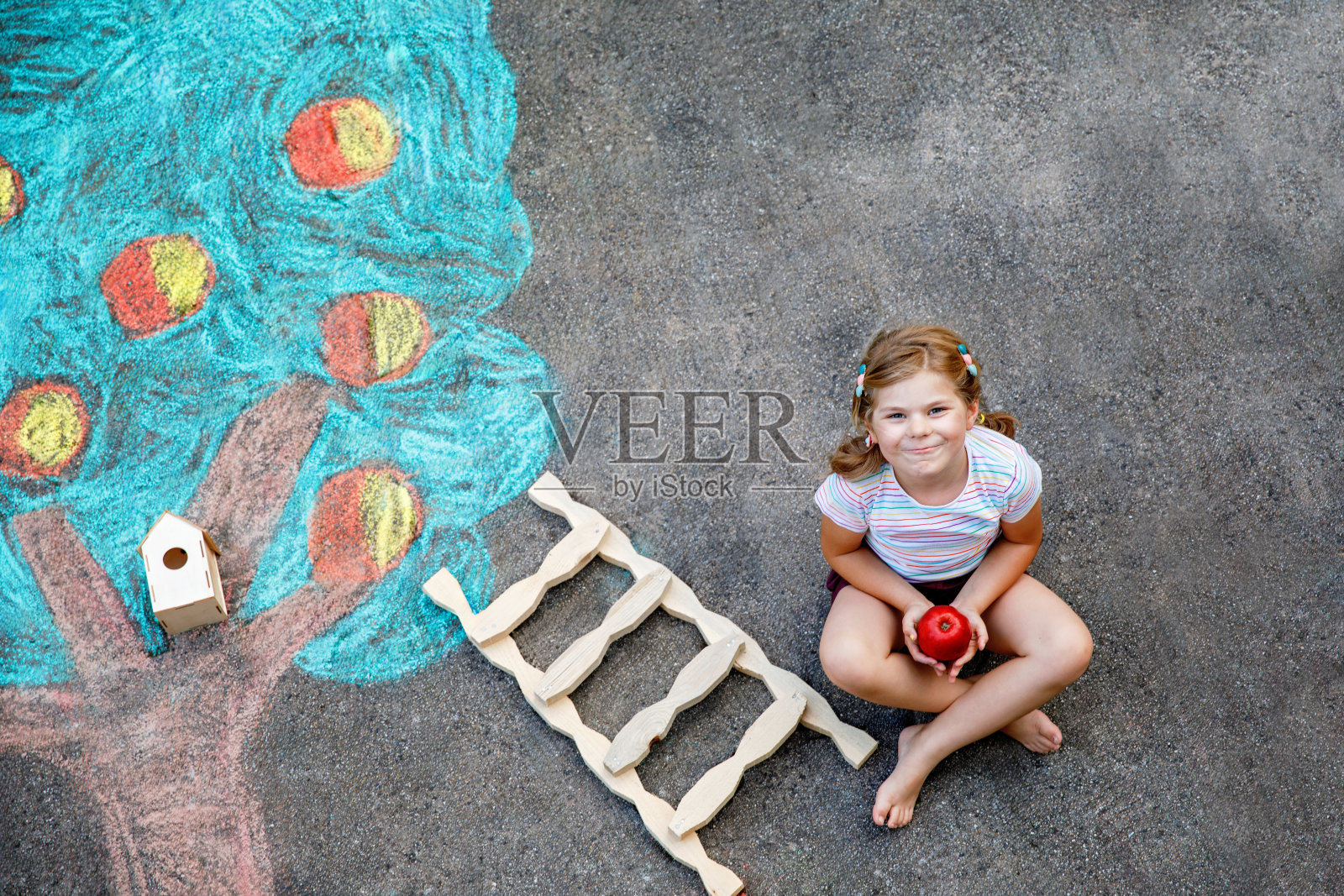 可爱的小女孩用彩色粉笔在柏油路上画苹果树上收获的苹果。可爱的学龄前儿童玩粉笔画。儿童创意休闲,写写画画。照片摄影图片
