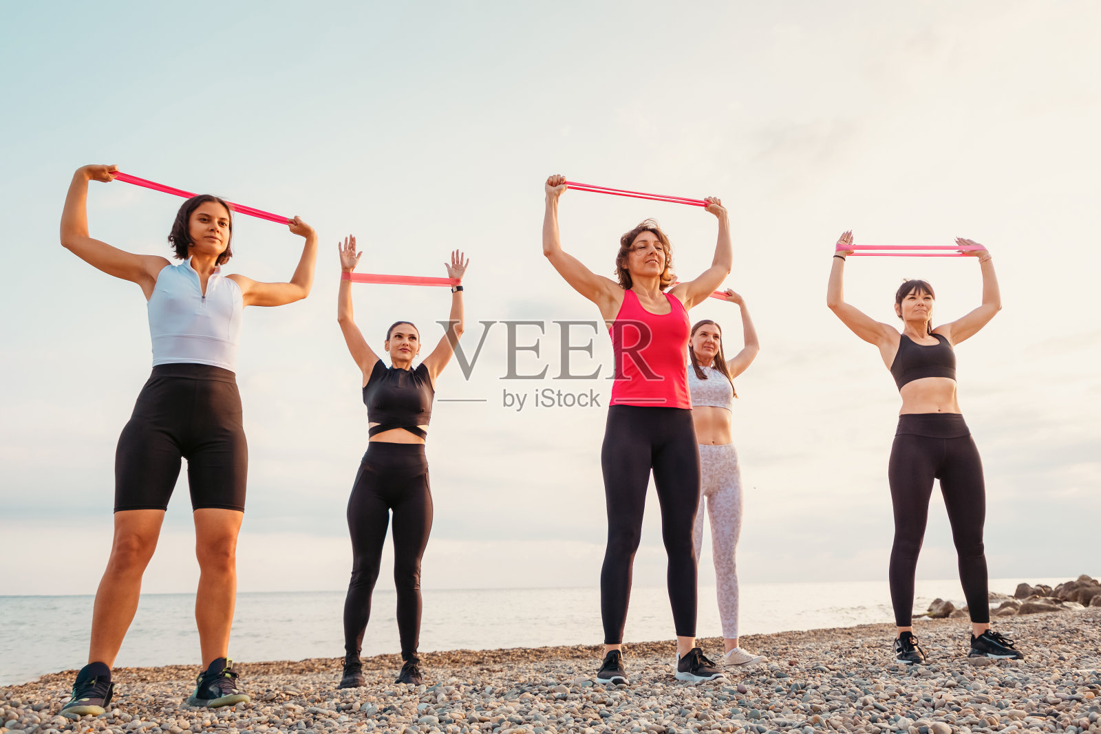 一群白种成年妇女正在沙滩上做运动和伸展运动。底部视图。健康生活方式的概念照片摄影图片