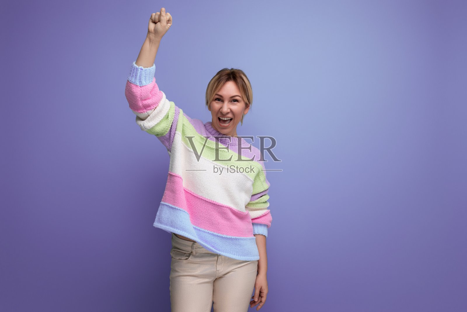 一位成功迷人的金发女郎在紫色的背景上把她的手握成拳头照片摄影图片