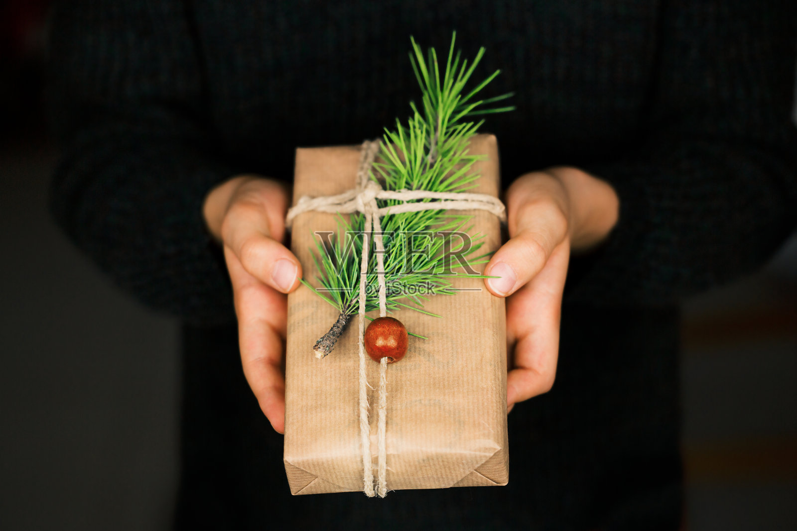手捧着用牛皮纸和松枝包裹的礼品盒照片摄影图片