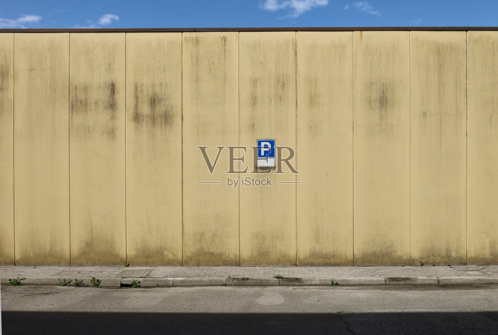 肮脏的预制混凝土墙,中间有停车标志。前面是铺着瓷砖的水泥人行道和街道,上面是蓝天照片摄影图片