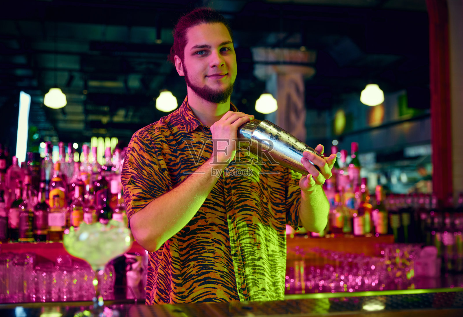 调酒师的肖像摇动鸡尾酒摇壶使酒精甜可口的鸡尾酒在酒吧与现代设计和霓虹灯照明。照片摄影图片