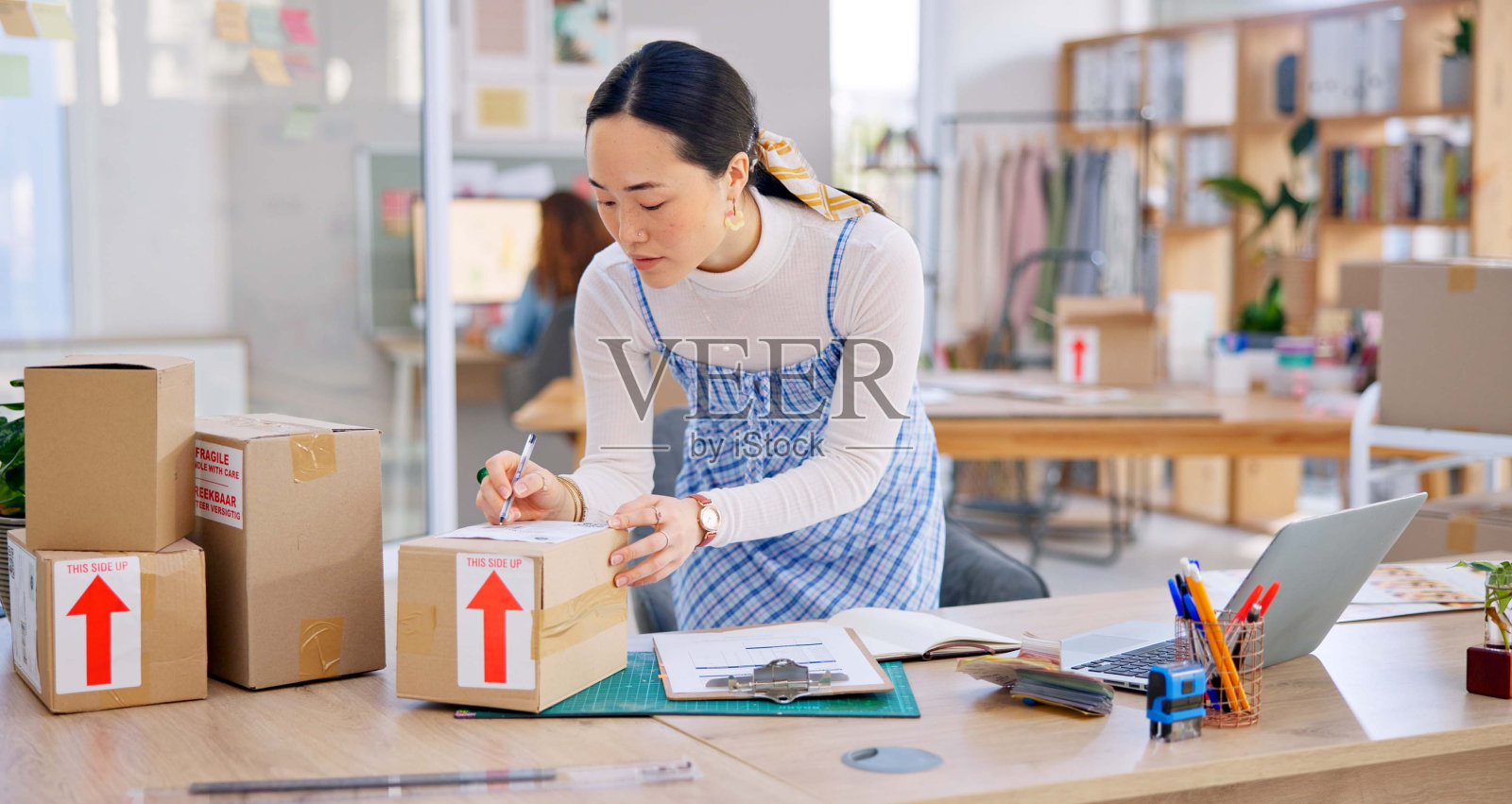电子商务,亚洲女性在笔记本电脑前拿着清单和盒子,在时尚初创公司阅读销售或库存信息。网上购物,送货和小企业主,库存清单为网上商店包裹检查。照片摄影图片