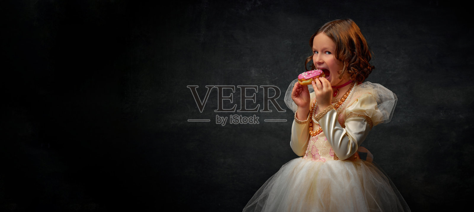 横幅。一个中世纪的小女孩,穿着老式的服装,在复古的背景下咬着甜甜的甜甜圈。文本的负空间。照片摄影图片