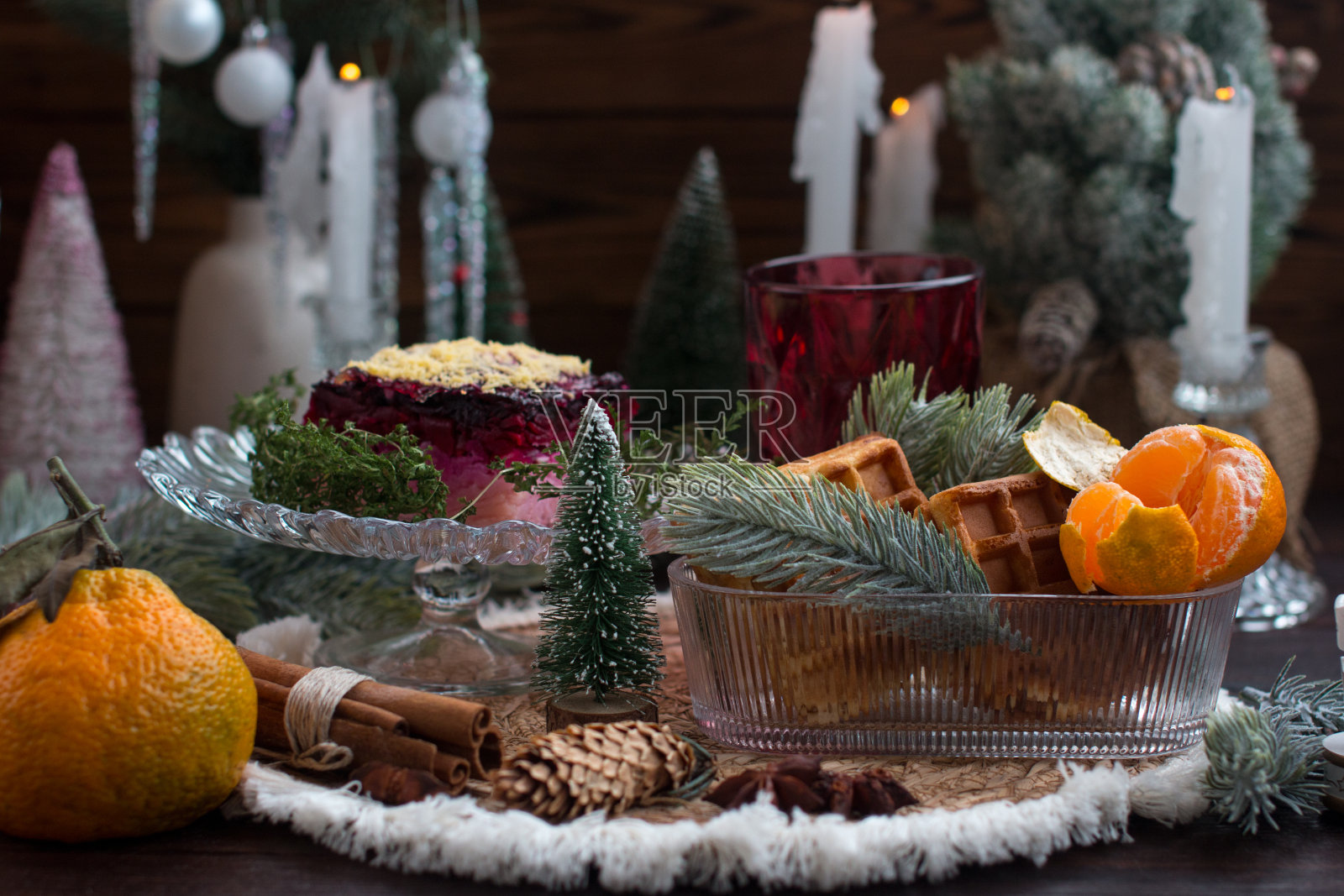 烛光下的年夜饭,皮大衣下的鲱鱼沙拉。节日餐桌上的橘子,用蓬松的云杉和球果装饰照片摄影图片