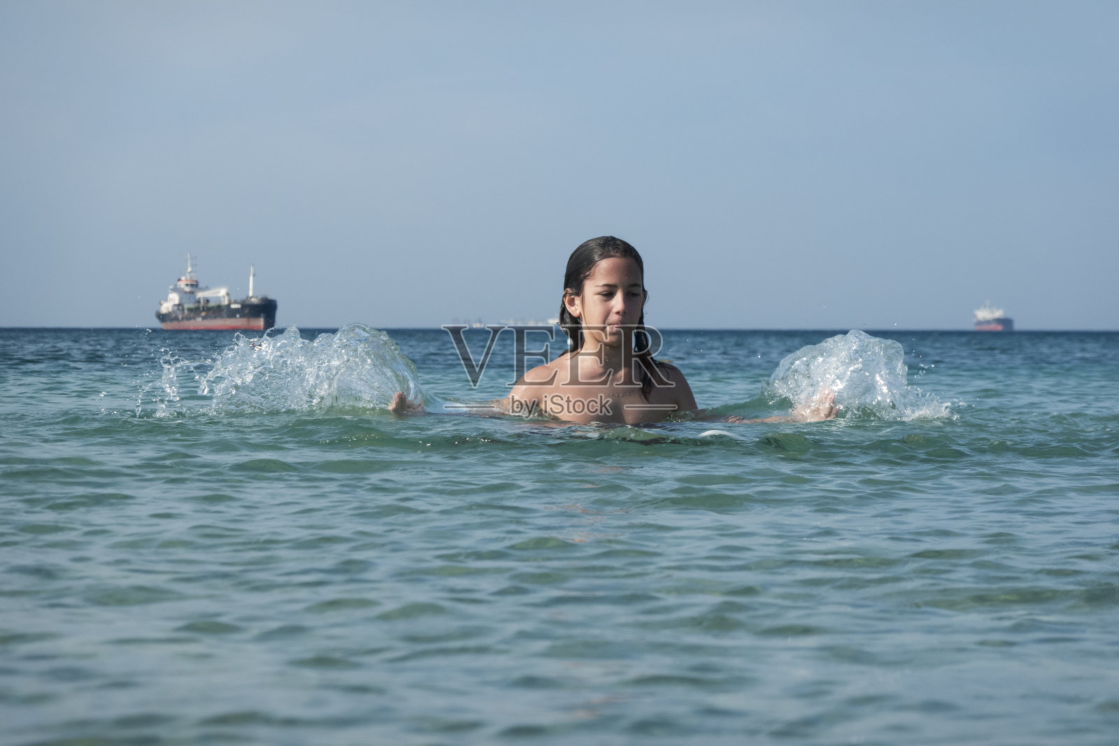他用手在海里泼水。一个夏天的早晨。忒涅多斯岛。爱琴海北部,12岁的帅哥。长头发的照片摄影图片