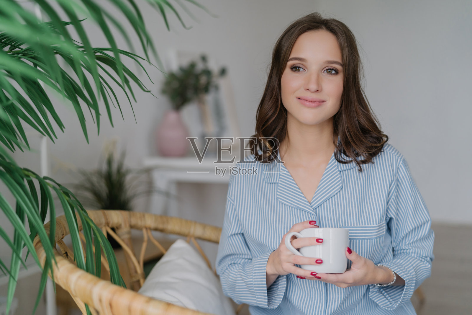 宁静的女人穿着条纹睡衣,带着马克杯,轻松的室内环境与绿色植物,体现宁静的家庭生活照片摄影图片