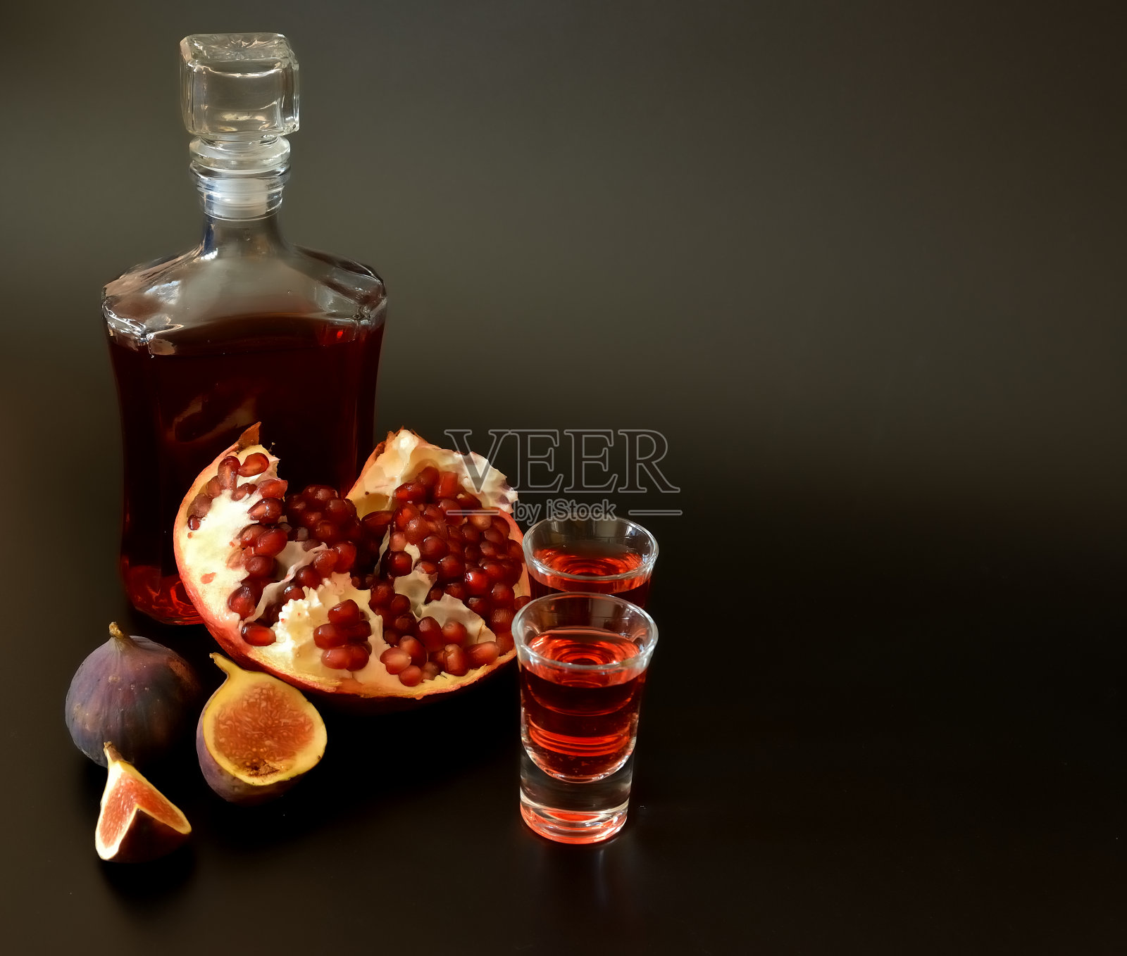 无花果石榴利口酒,黑色背景上的两杯一瓶自制酒,旁边是成熟的水果。照片摄影图片