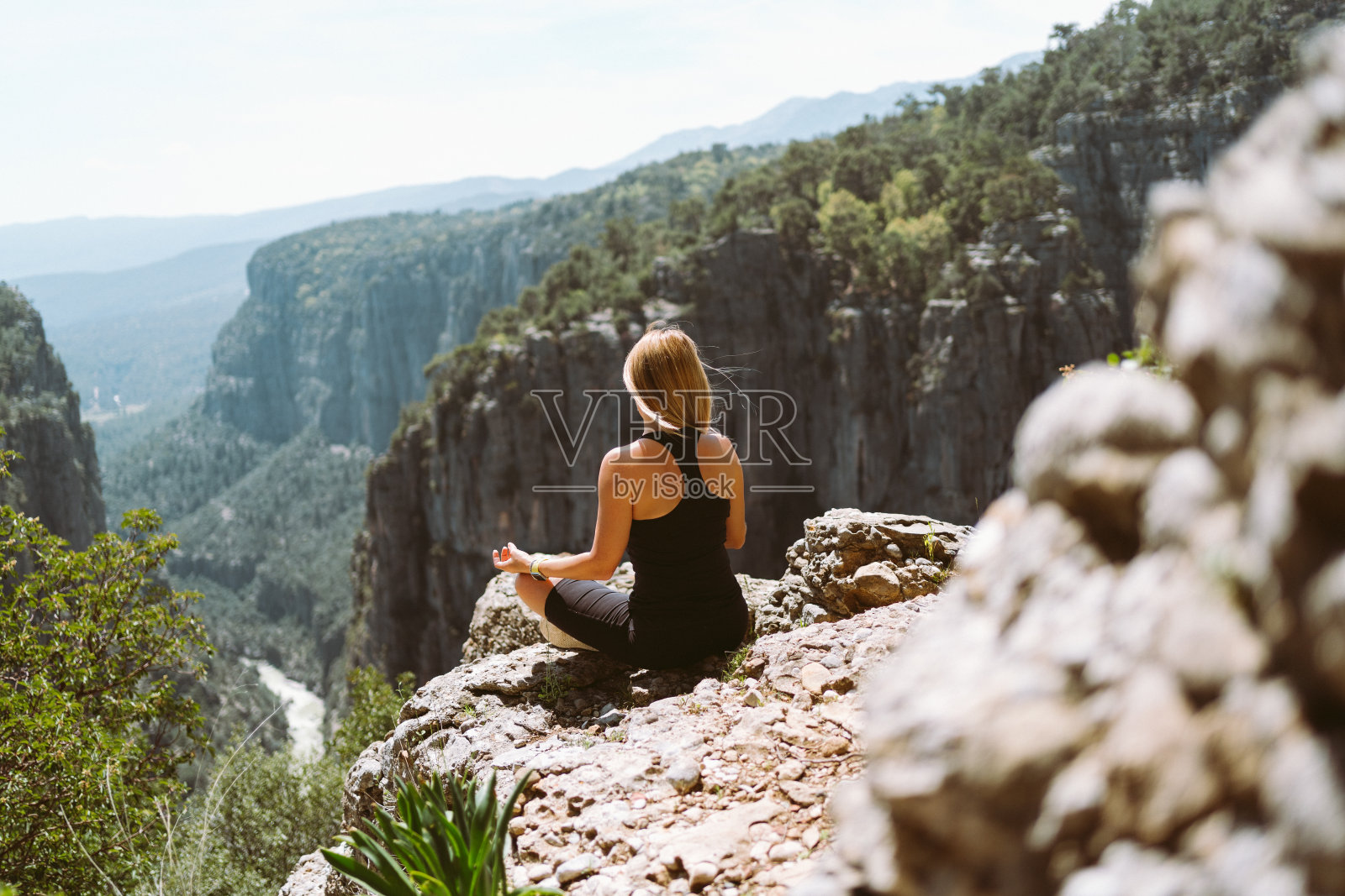 年轻美丽的女孩女人在黑色运动苗条的衣服冥想边缘岩石山悬崖峰与山谷峡谷的看法。从后面看,一位健康的女徒步旅行者到达了山顶照片摄影图片