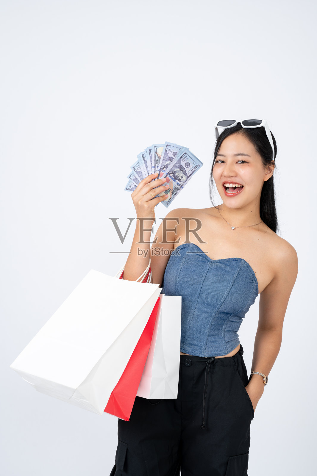 优雅的亚洲女人穿着时髦的衣服,拿着购物袋和现金,背景是孤立的白色照片摄影图片