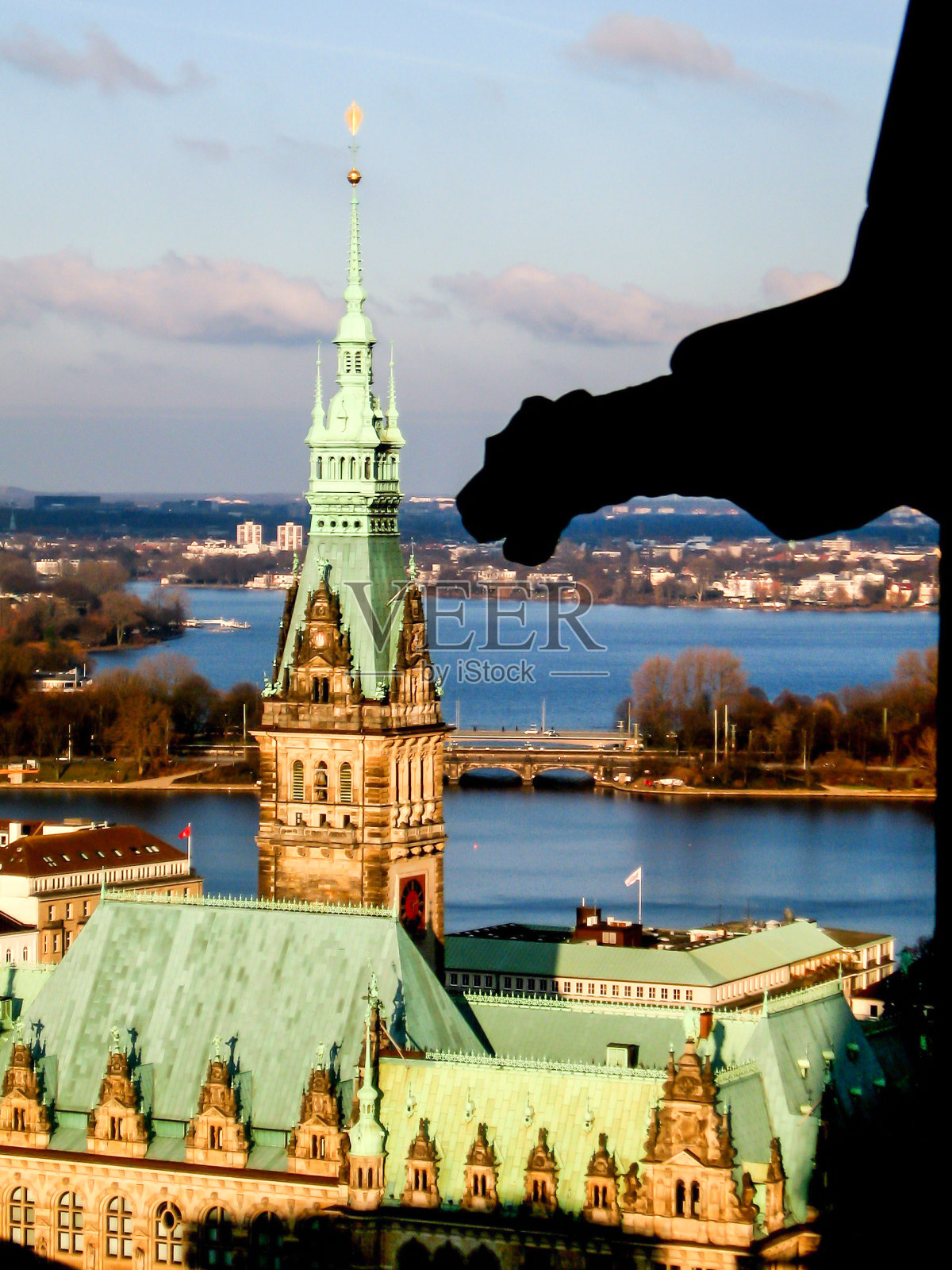 从圣尼古拉斯教堂残破的塔尖上可以看到美丽的新文艺复兴风格的汉堡市政厅,以及前景中一个石像鬼的剪影。汉堡市政厅建于19世纪,以表达城市的富裕和繁荣照片摄影图片