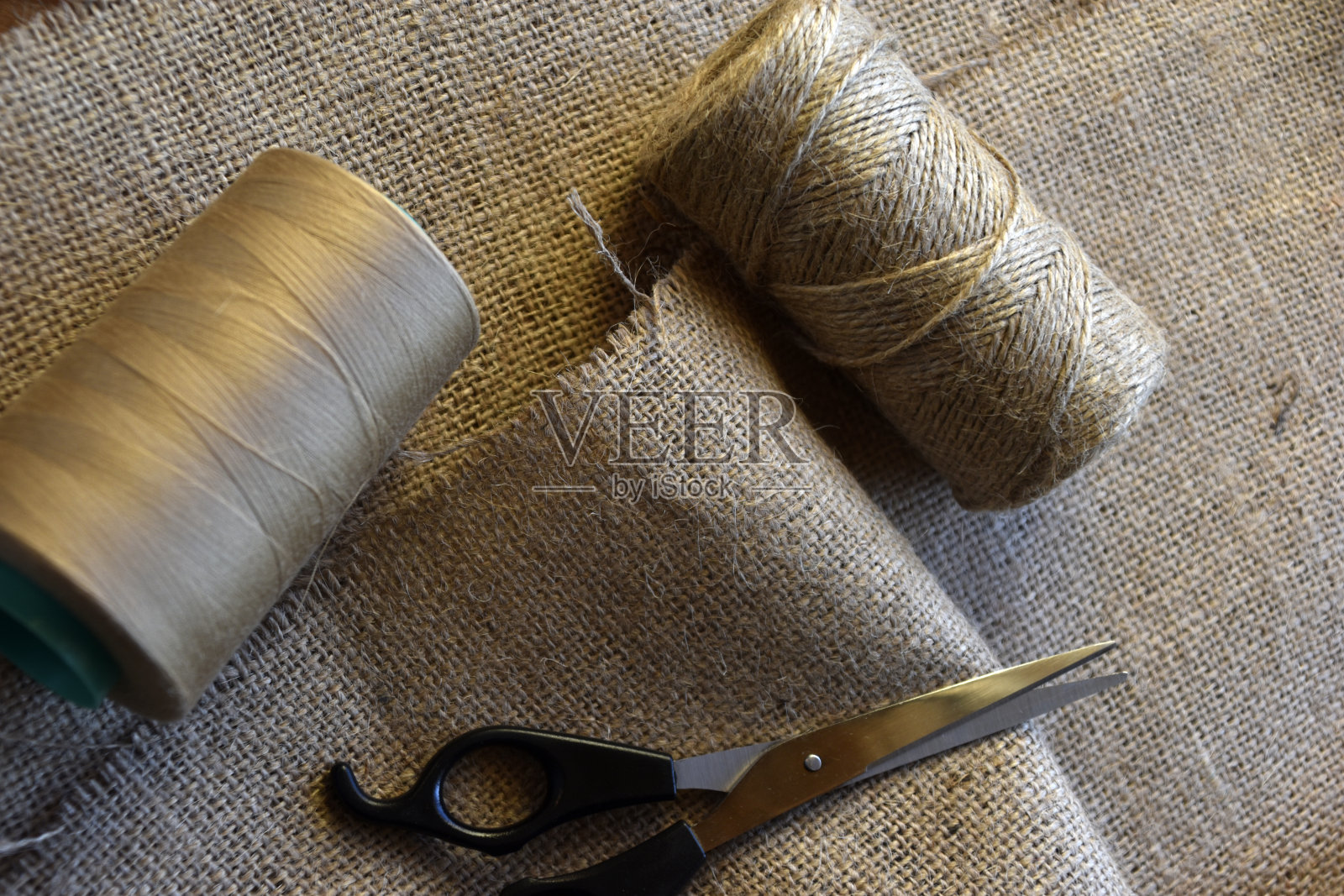 黄线和剪刀在粗麻布的背景上。黄色粗布线和剪刀。照片摄影图片