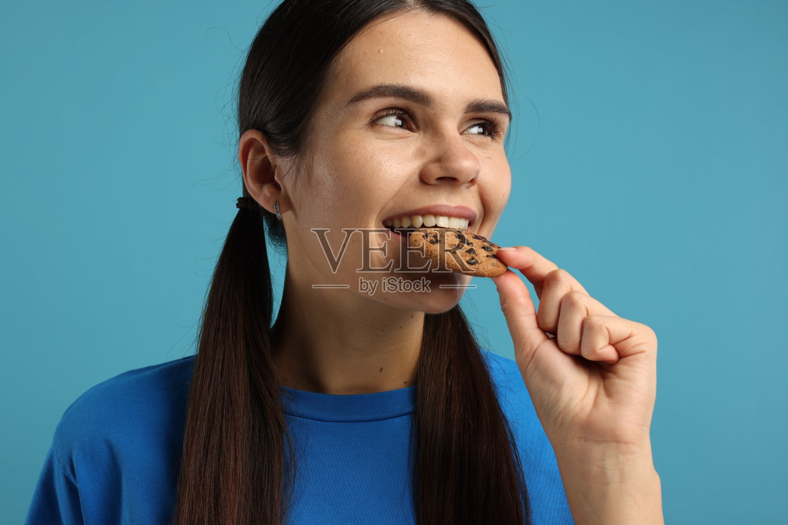 年轻女子拿着浅蓝色背景的巧克力曲奇,特写照片摄影图片