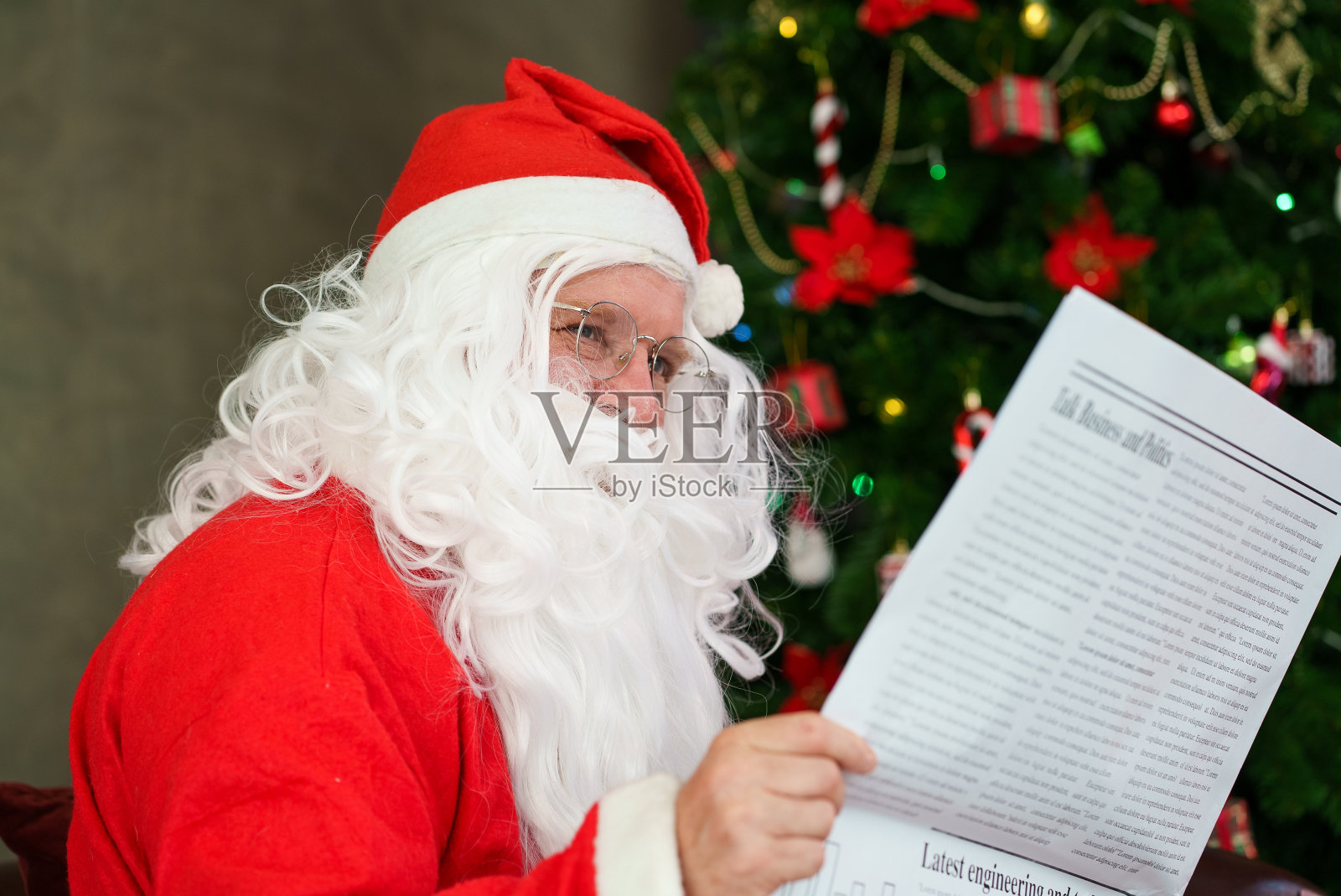 穿着圣诞老人服装的老人坐在家里客厅的沙发上看报纸照片摄影图片