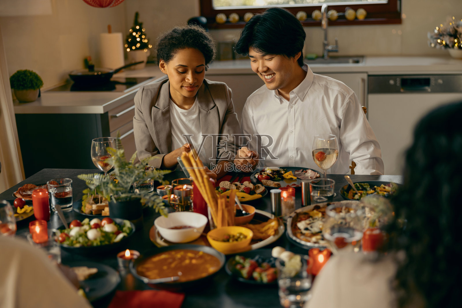 微笑的男人和女人坐在家里的节日餐桌旁,边吃边看手机照片摄影图片