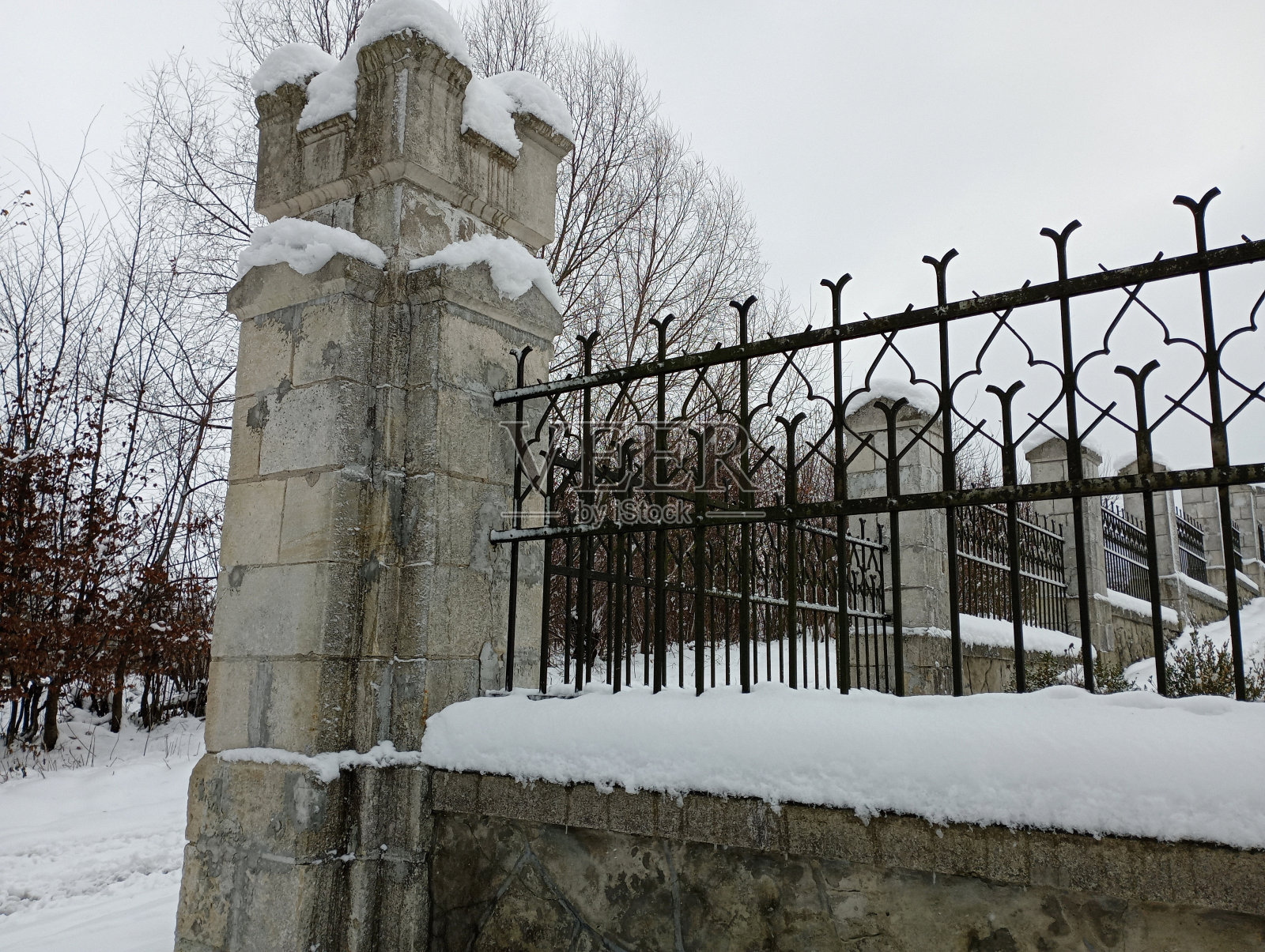 有砖柱和金属隔板的古老栅栏。冬季景观和古老的栅栏在冬天被雪覆盖。照片摄影图片