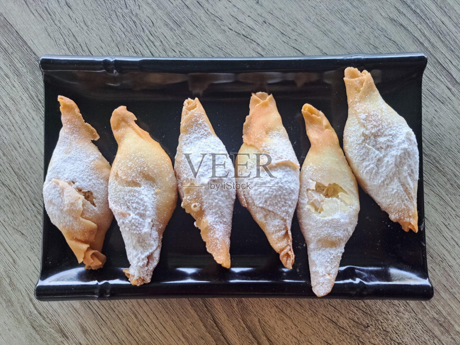 美味的Pisang Molen或油炸香蕉Molen脆撒糖粉在盘子里。小吃菜单。俯视图照片摄影图片