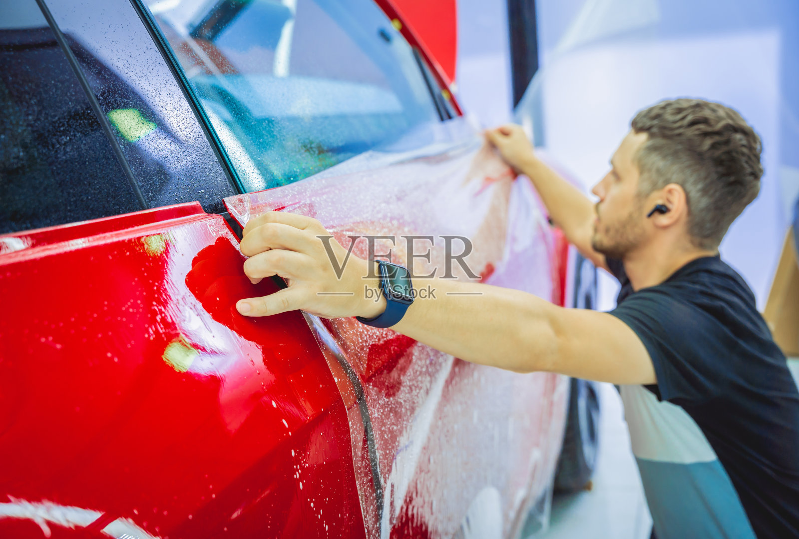 在新红色汽车上安装保护膜的过程。照片摄影图片