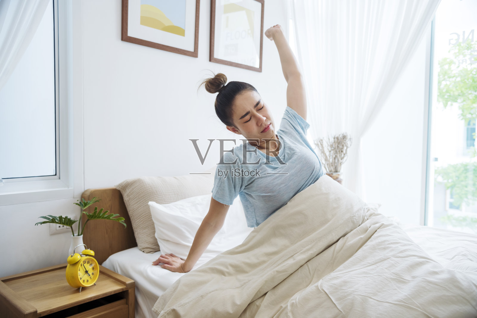 亚洲女性在白色舒适的卧室里醒来,享受清晨日出的快乐时光。美丽的中国人使用手动停止时间闹钟。快乐的人生活方式早上醒来健康放松困倦打盹照片摄影图片