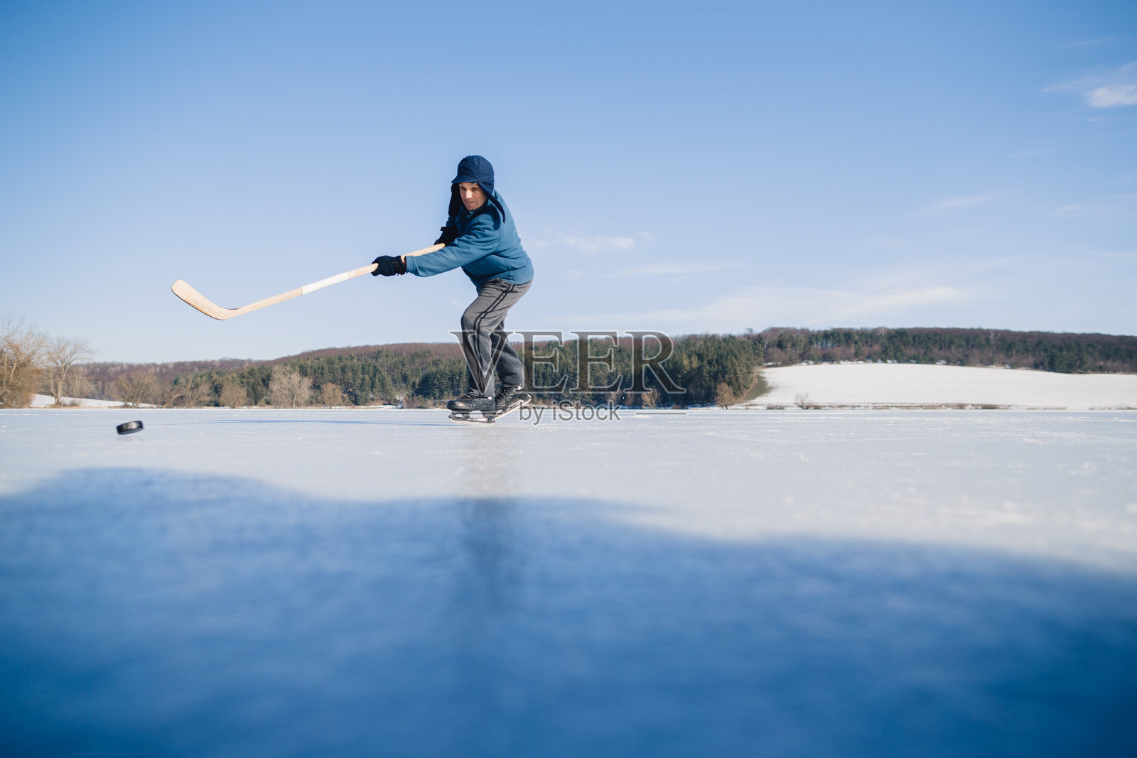一位年长的男人在冬天结冰的湖面上练习用曲棍球杆击打冰球照片摄影图片