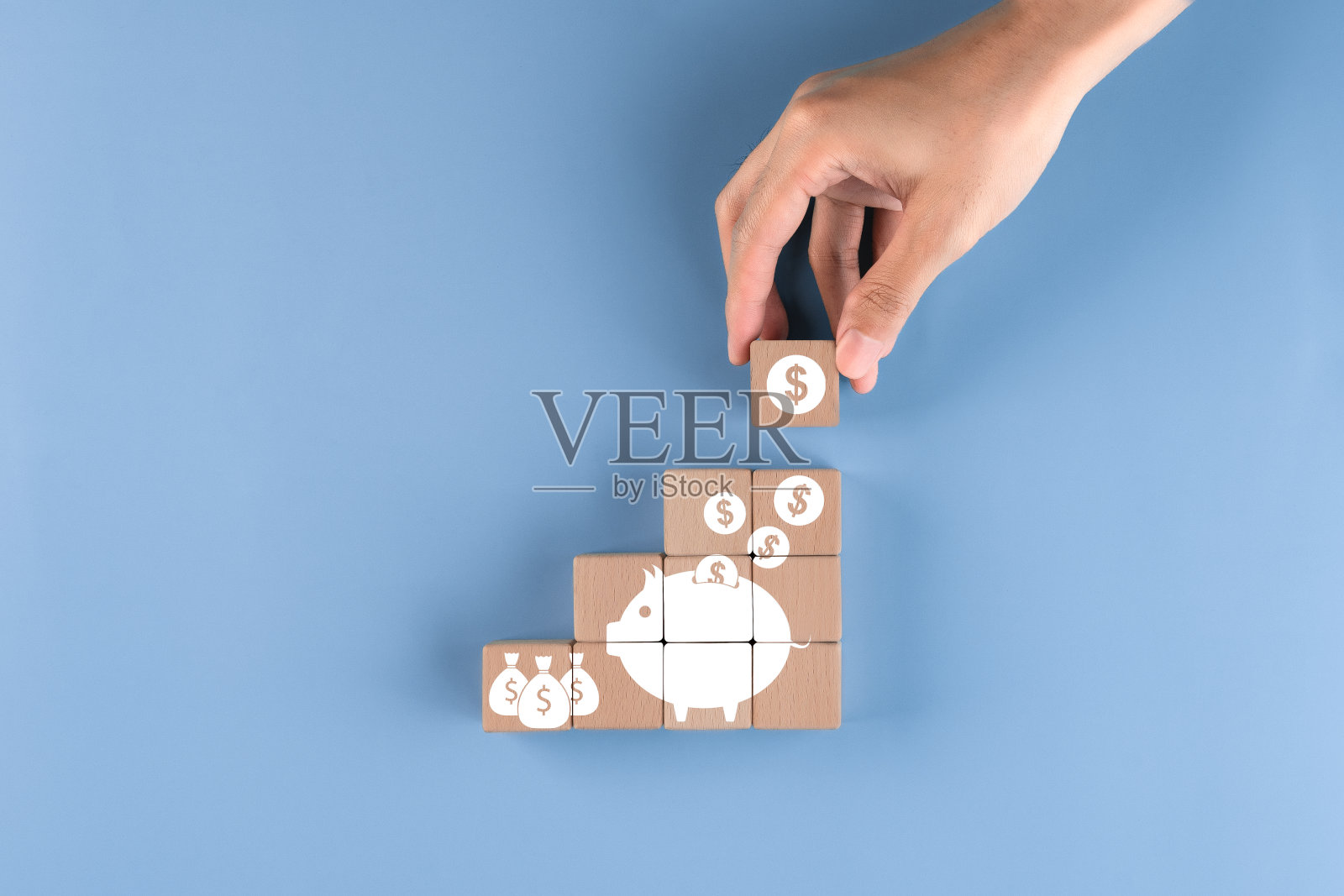 省钱理念:用手将木块放在蓝色背景上存钱,为投资攒钱,把硬币放进存钱罐里。照片摄影图片