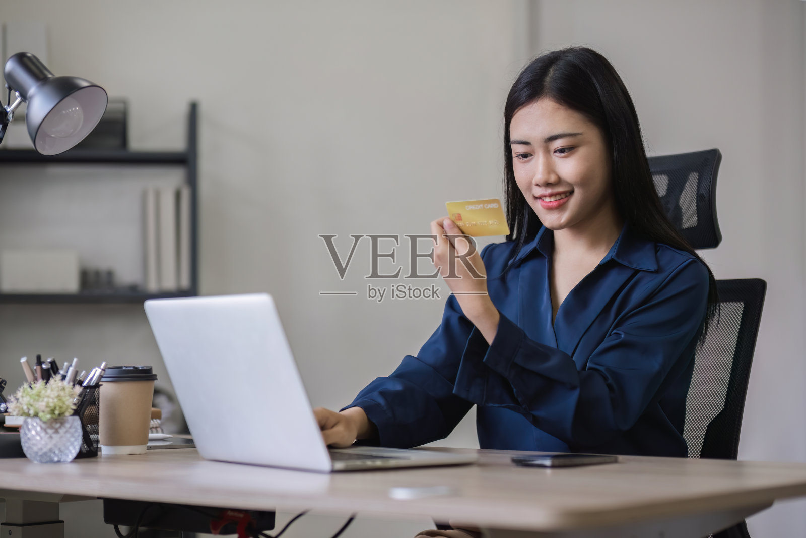 年轻女子手持信用卡,用笔记本电脑在网上购物,并通过智能手机上的应用程序在线支付照片摄影图片