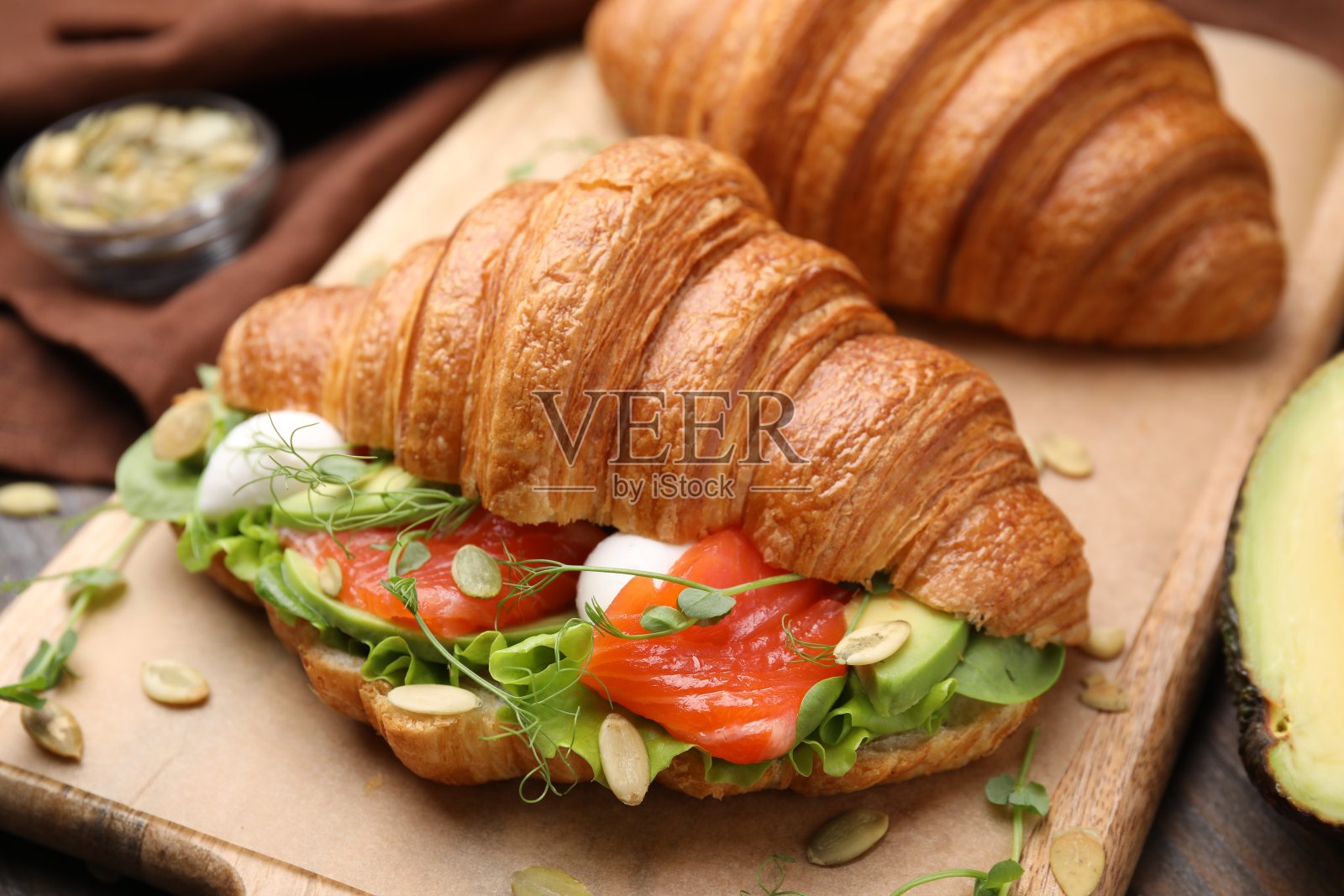 木桌上美味的牛角面包配鲑鱼、牛油果、马苏里拉奶酪和生菜,特写照片摄影图片