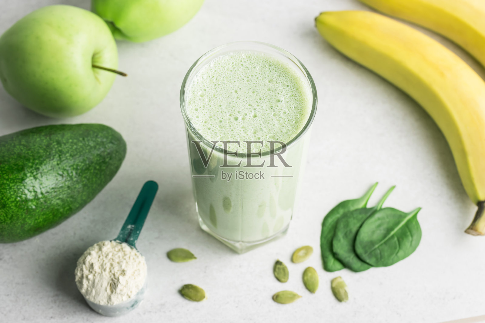 绿色排毒奶昔,混合素食饮料,蛋白质奶昔在一个杯子里的菠菜,香蕉,苹果,鳄梨和种子在一个桌子上,健康的饮食理念照片摄影图片
