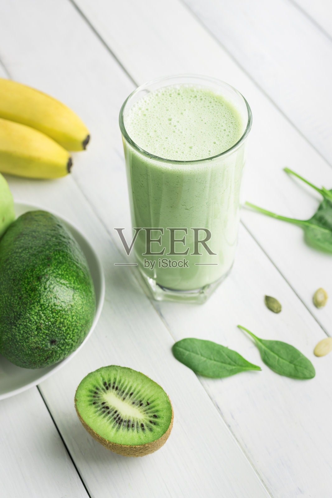 绿色排毒奶昔,将菠菜、苹果、香蕉、猕猴桃、鳄梨和种子放在白色木桌上,混合在一起的素食饮料,健康的饮食理念照片摄影图片