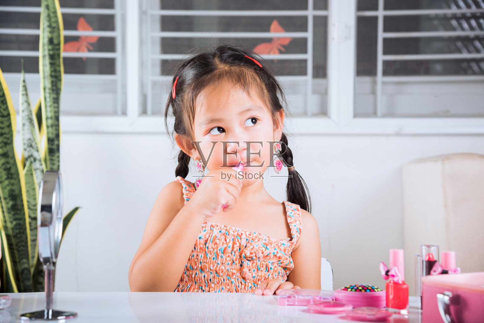 小女孩正在化妆,她看着镜子,把红色的口红涂在嘴里照片摄影图片