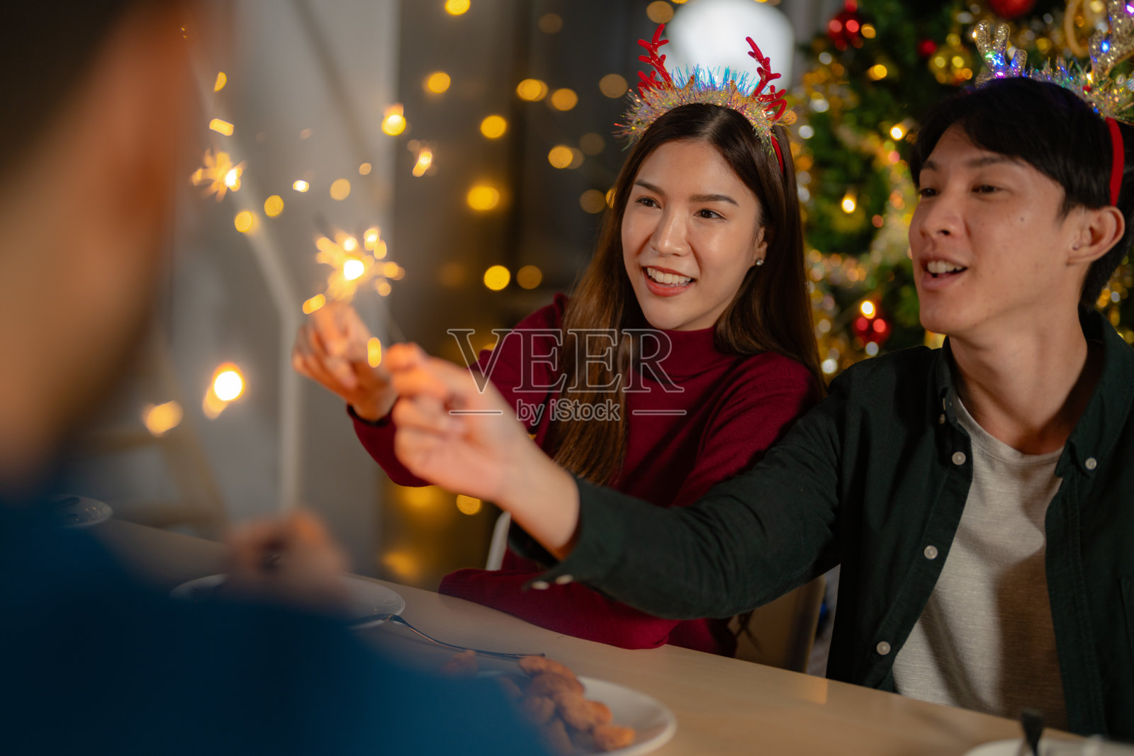 男男女女在一个有圣诞树的聚会上拿着烟花。年轻夫妇亚洲人喜欢庆祝圣诞节和新年。欢天喜地,用美食、美酒和友谊为爱庆祝;照片摄影图片