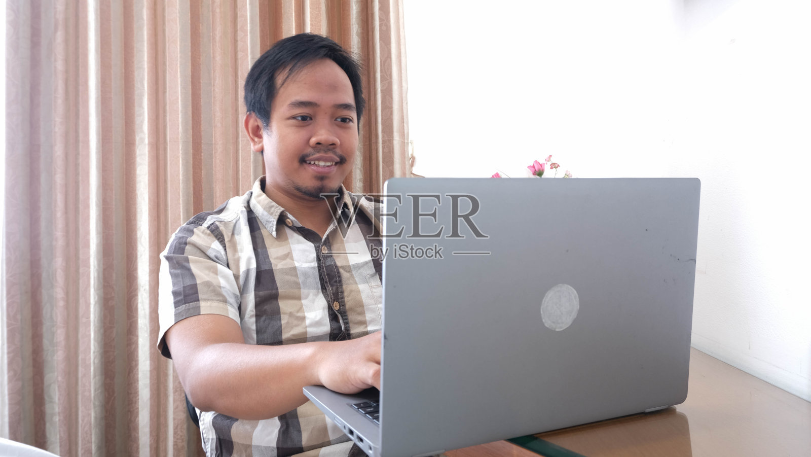 东南亚男人微笑着在笔记本电脑上打字,灵活工作的概念照片摄影图片
