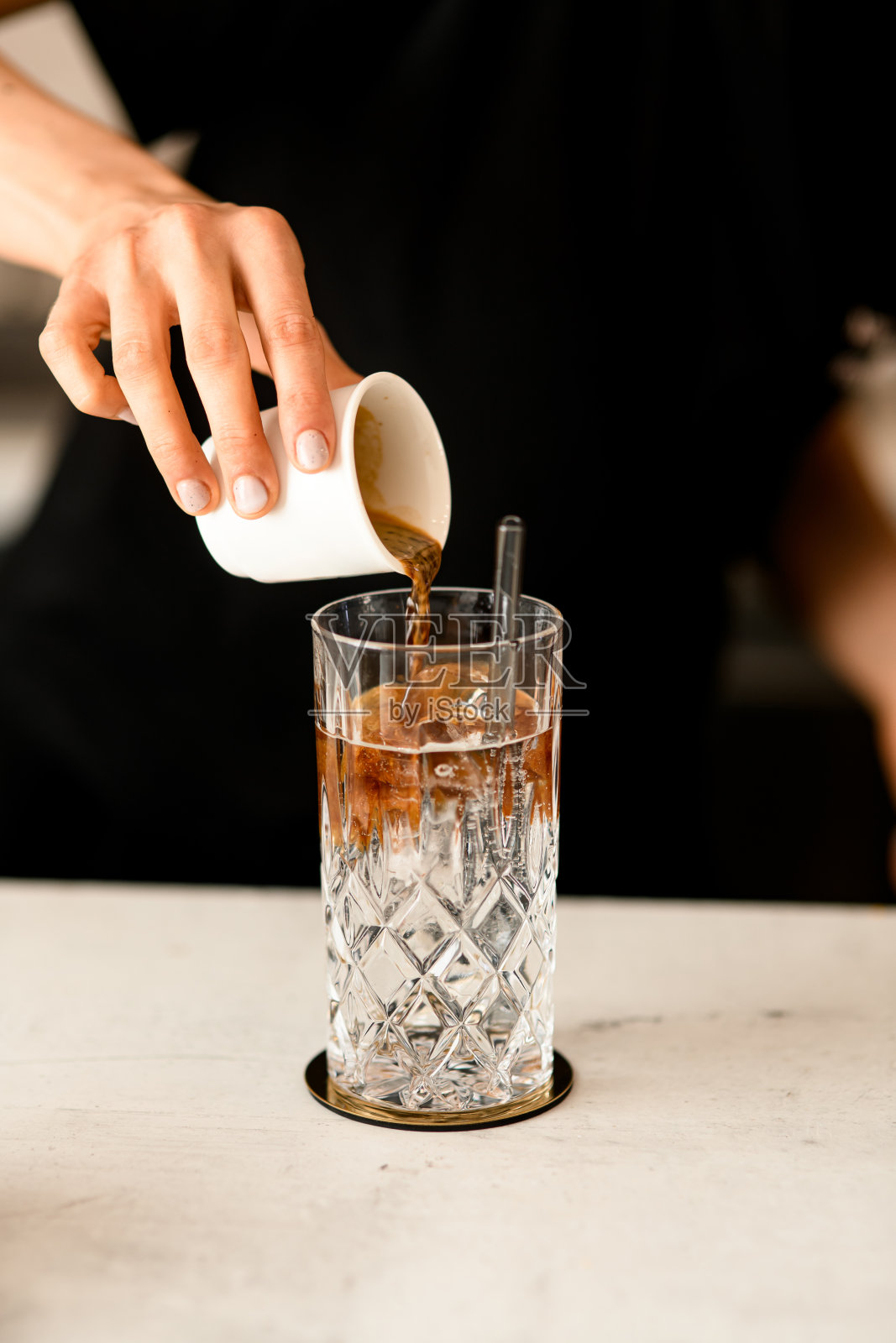 在咖啡馆或餐厅的餐桌上,咖啡师将咖啡倒入冰块中,并配上汤力水照片摄影图片