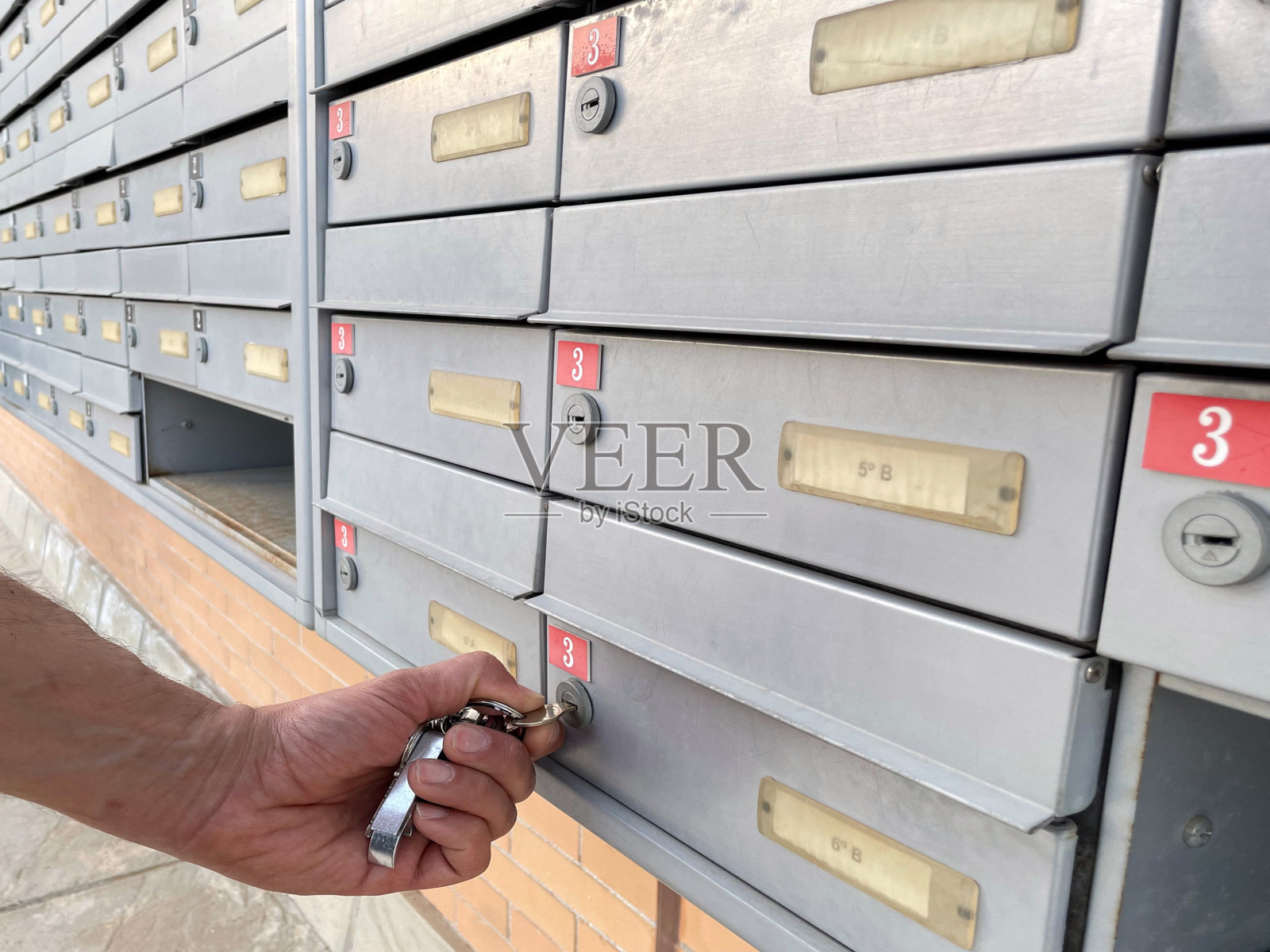 一个人用钥匙打开户外社区邮箱的手。照片摄影图片