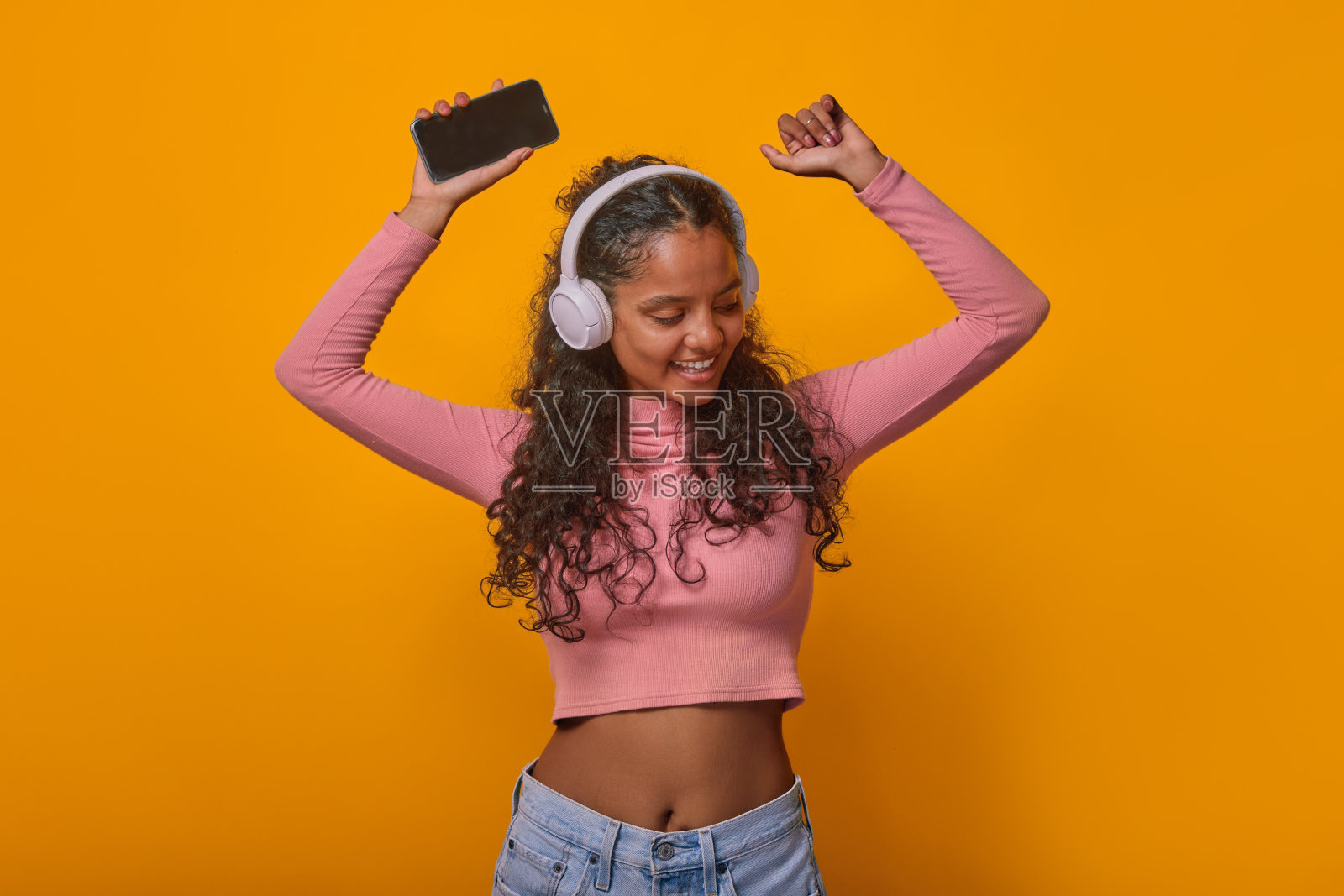 年轻跳舞的印度少女戴着耳机听音乐,拿着手机照片摄影图片