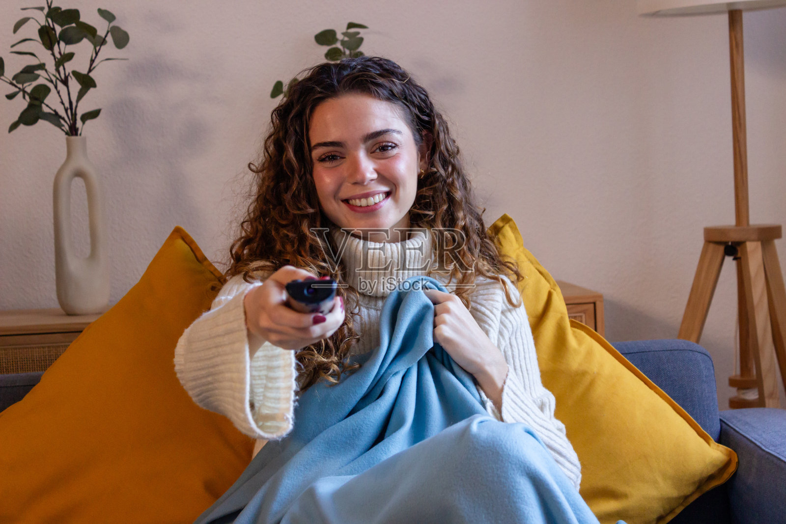 微笑的年轻女子坐在沙发上,拿着客厅的遥控器照片摄影图片