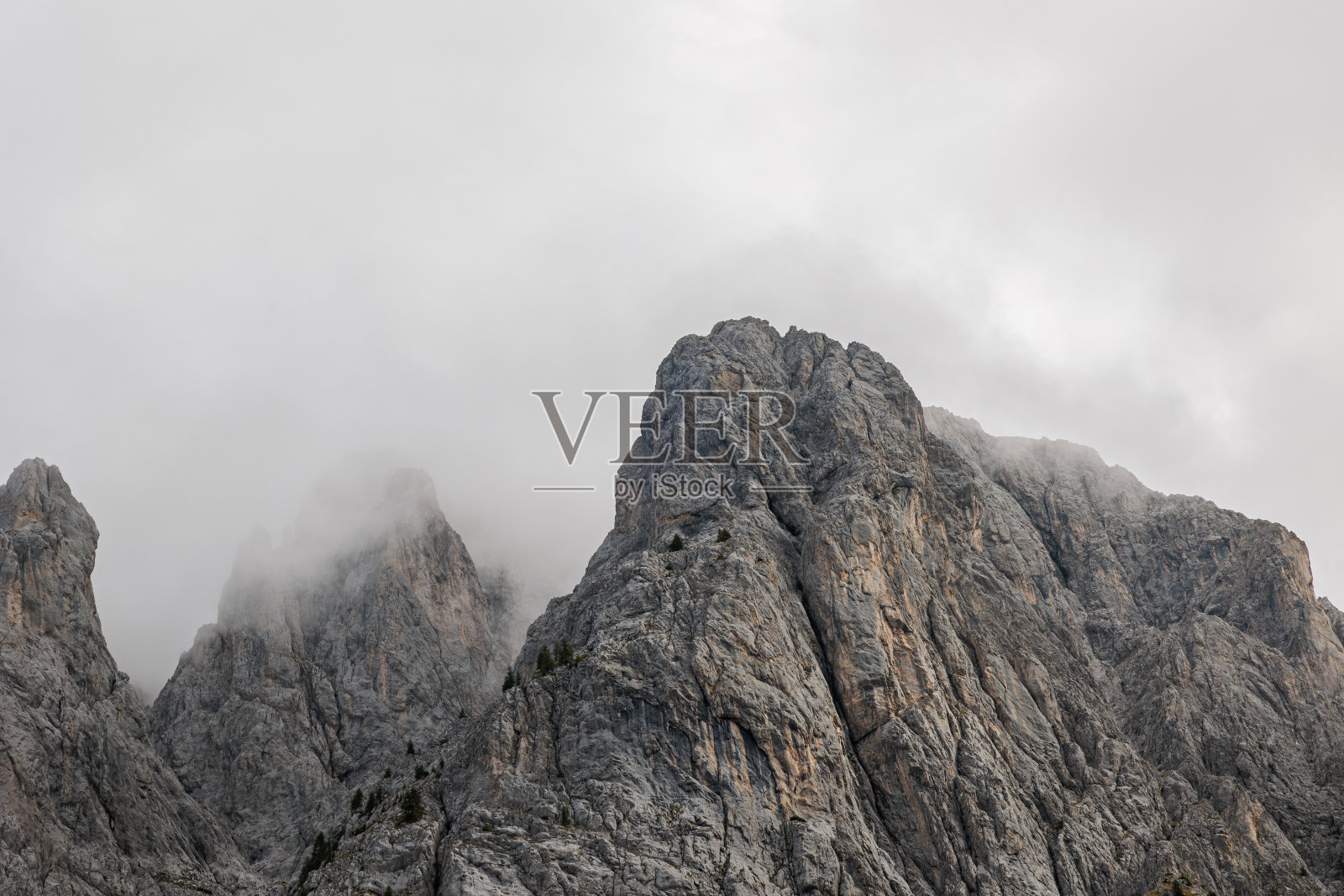 从下面看一座雄伟的山的陡峭的岩石斜坡,部分被云覆盖照片摄影图片