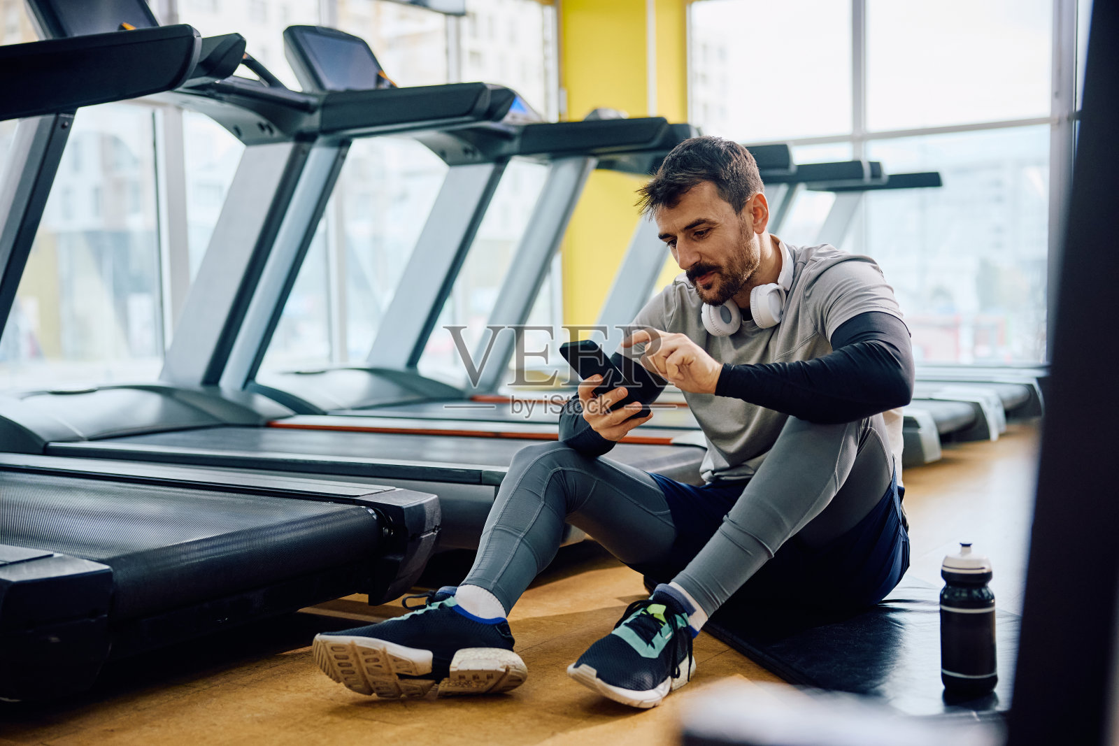 男运动员在健身房喝水休息时发短信。照片摄影图片