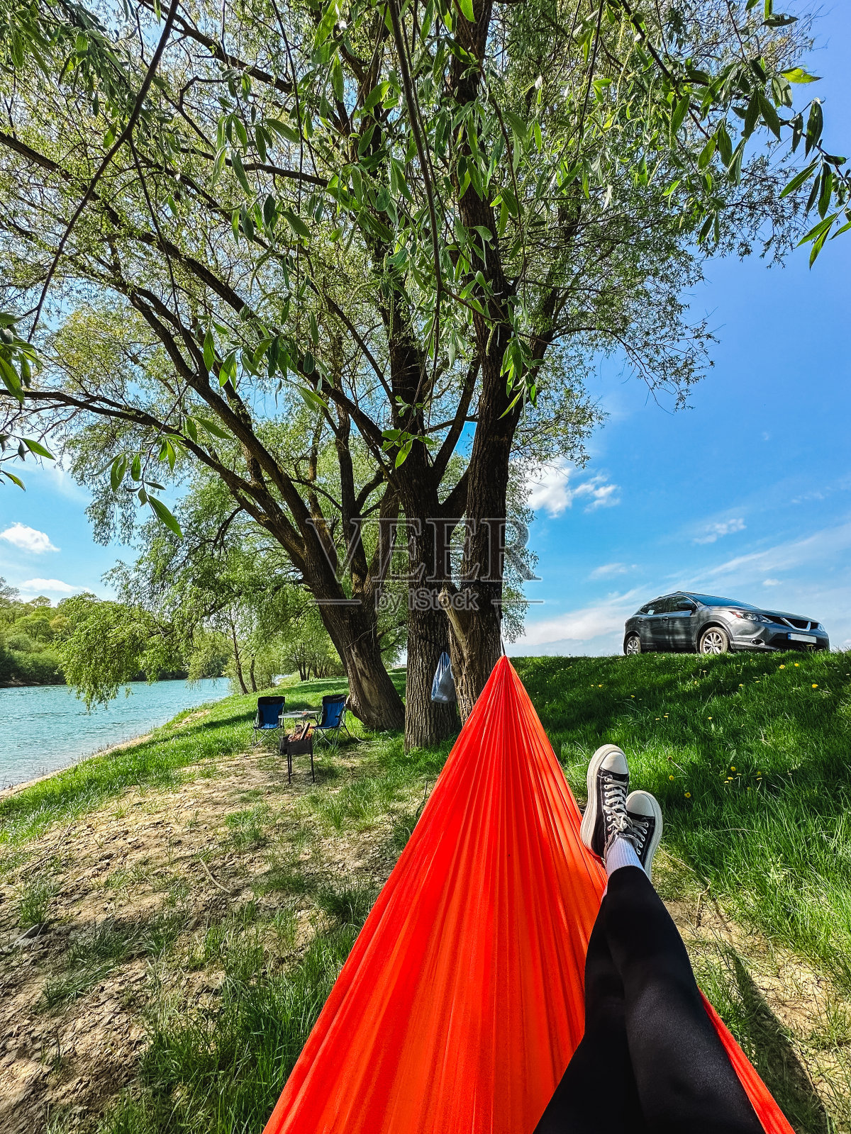 一个女人躺在吊床上,俯瞰着一条河,河岸边停着一辆车。照片摄影图片